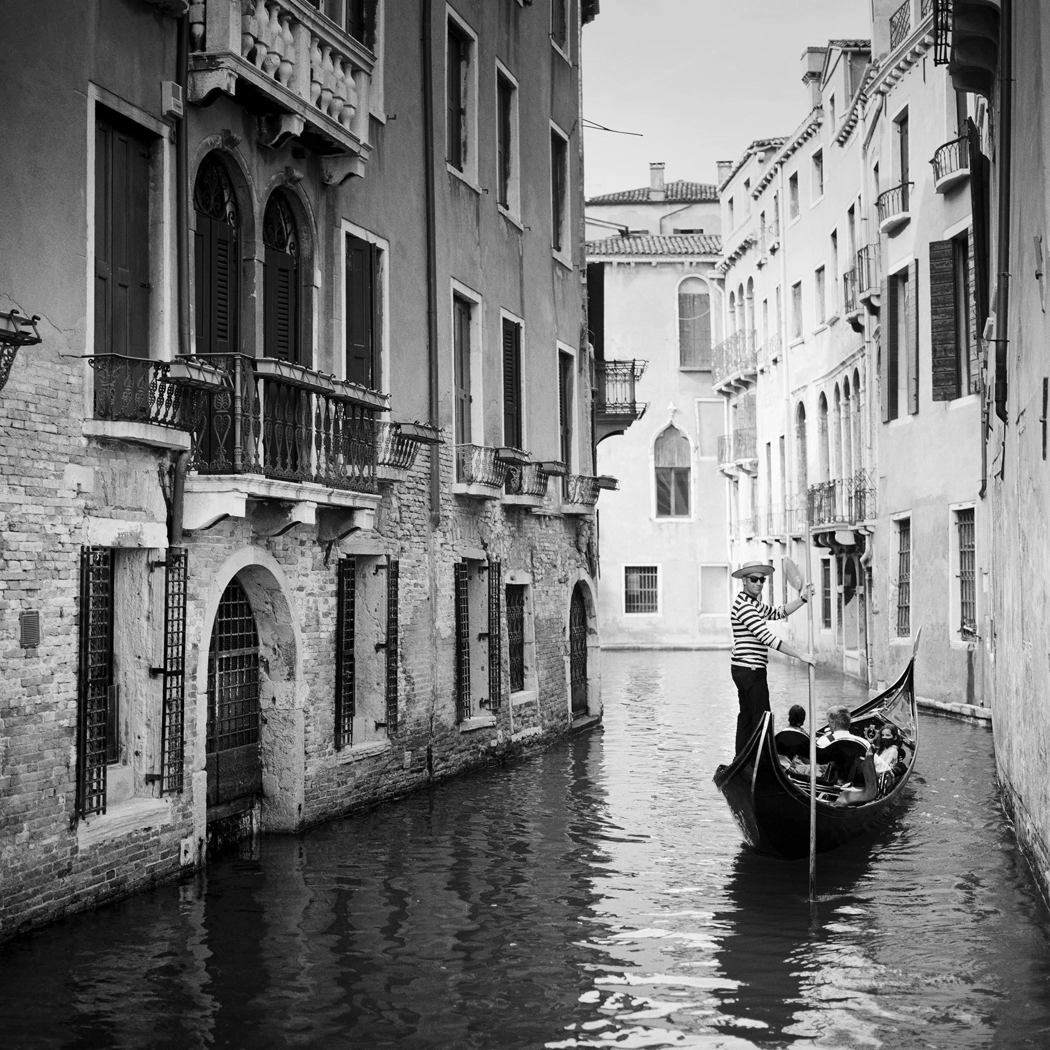 Black-and-white photograph of a gondolier navigating a narrow canal in Venice, by Gerald Berghammer.