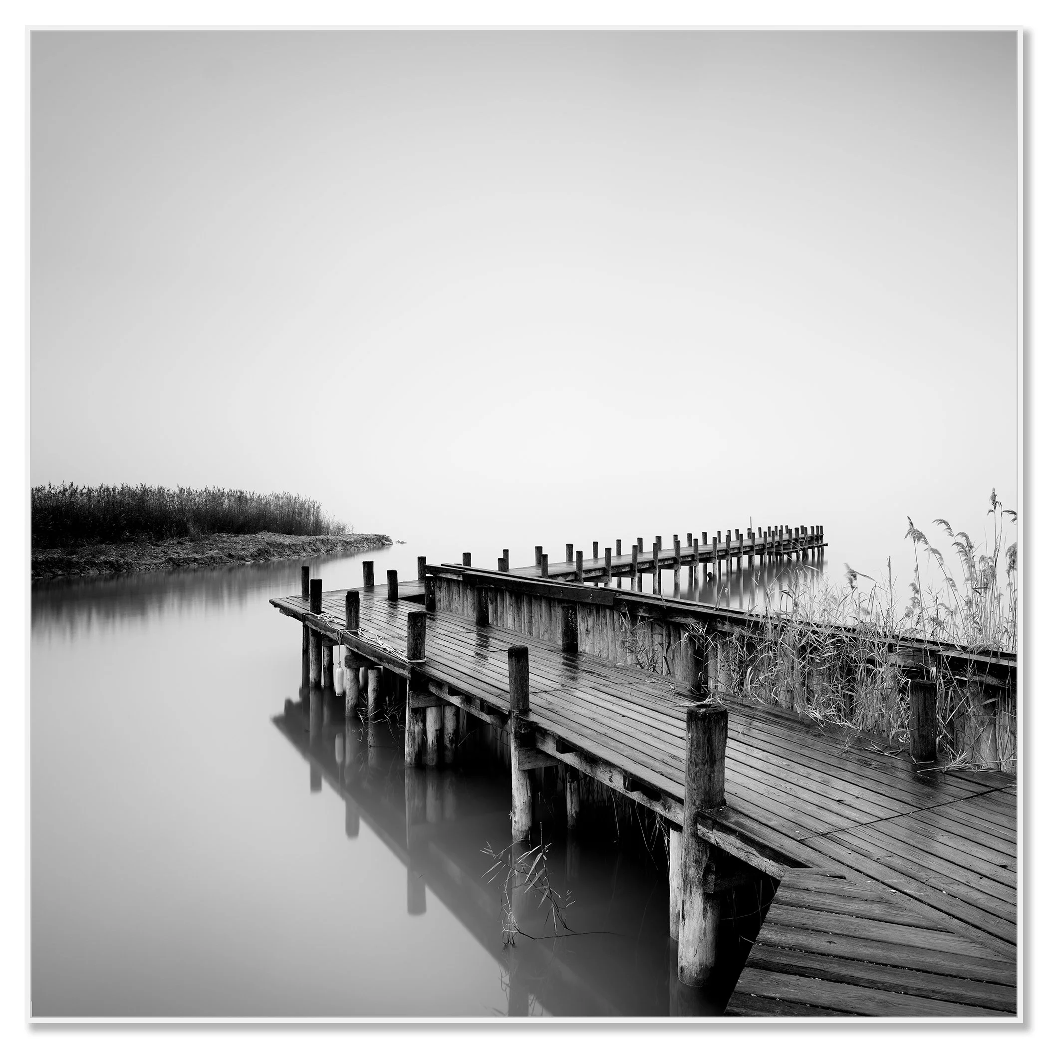 Minimalist black and white wall art showing a wooden jetty on still water with reeds at the edge – framed ArtBox white