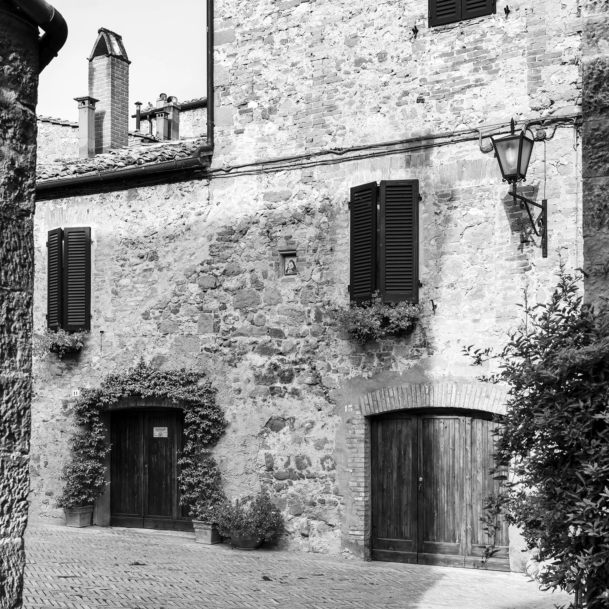 Gerald Berghammer - Black and white cityscape photography. Old stone building with wooden shutters, potted plants and outdoor seating in a narrow courtyard. Print detail 3