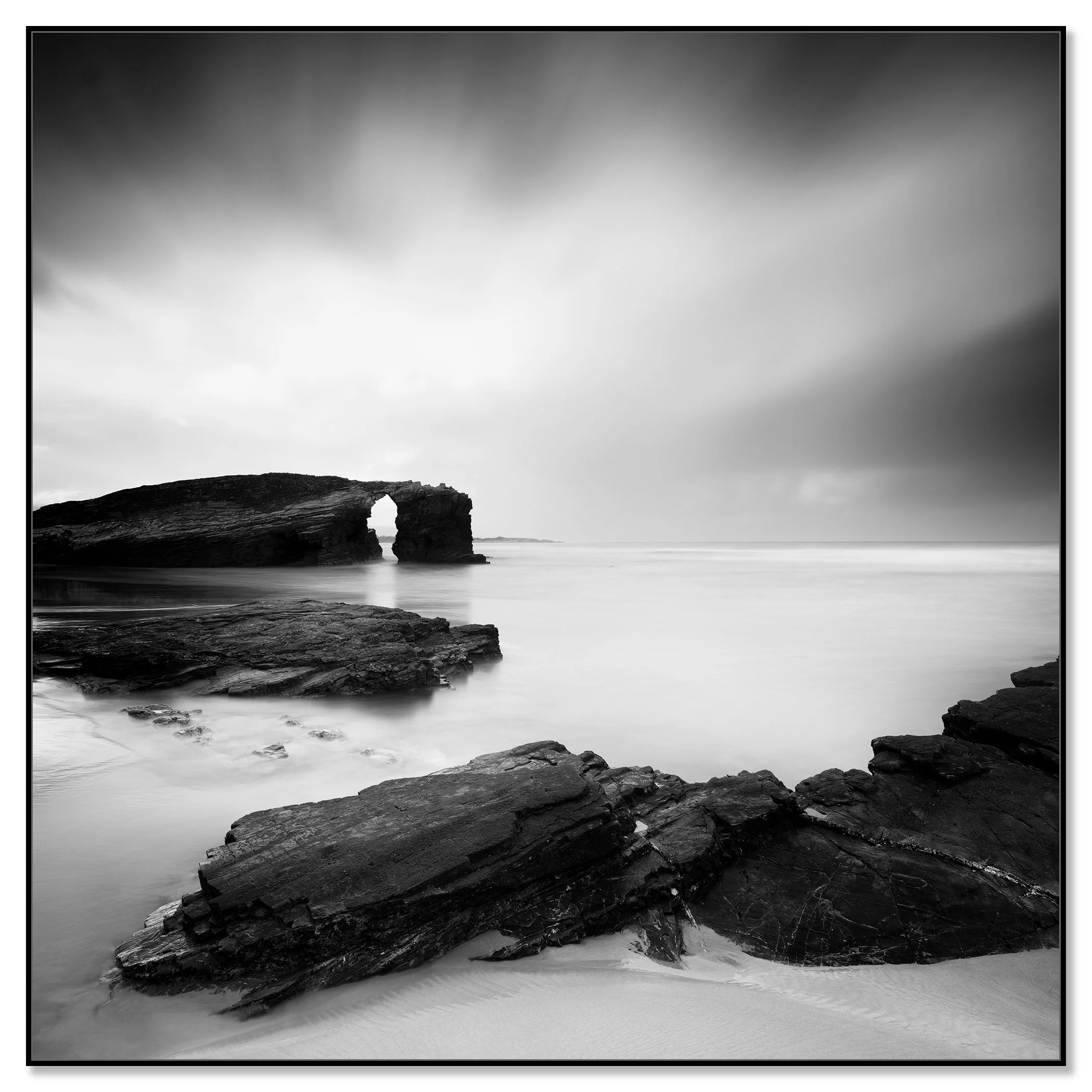 As Catedrais Beach rock arch in black-and-white, rocky shoreline and calm sea under a cloudy sky – framed ArtBox black
