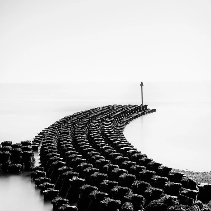 Cobbolds Point Study 1 by Gerald Berghammer, minimalist black-and-white photograph of coastal groynes extending into calm water in England.