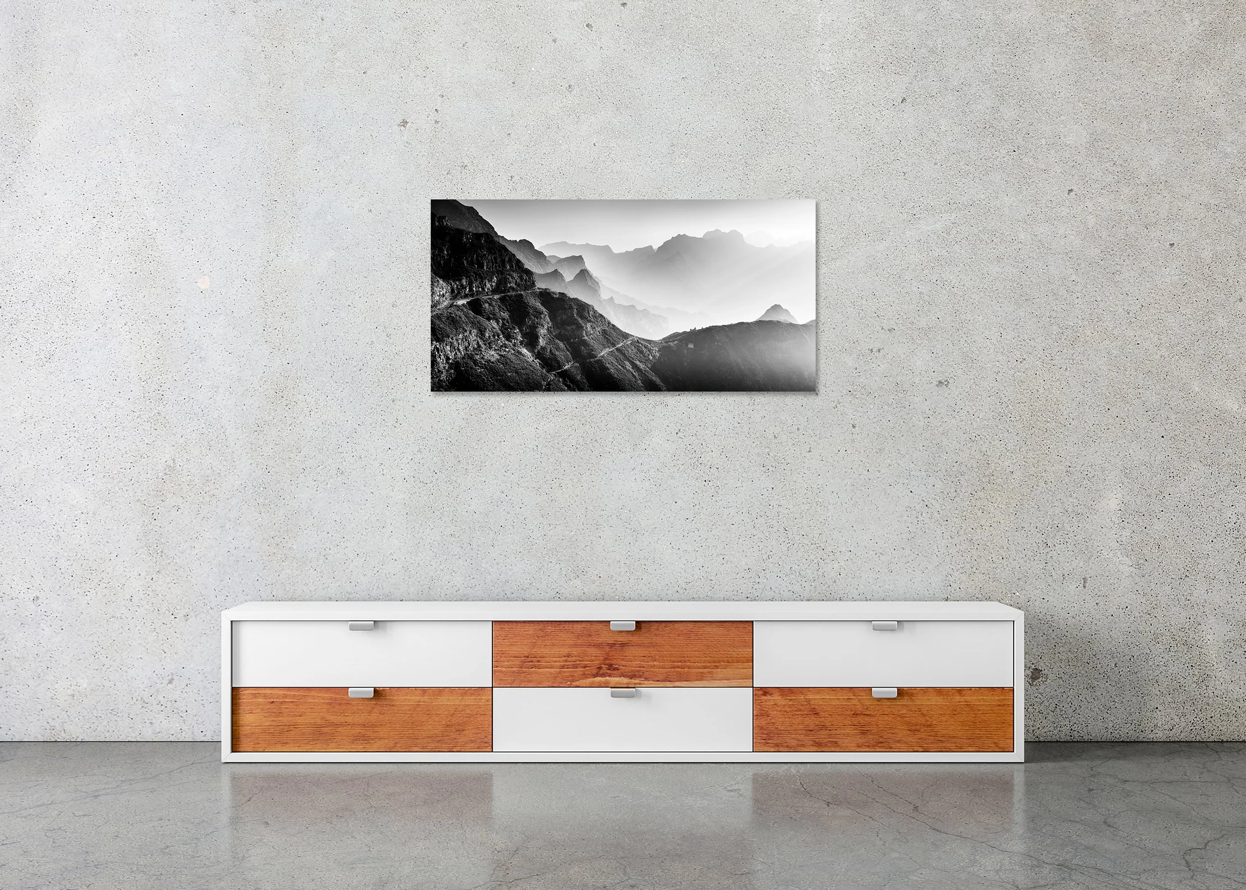 Frameless ChromaLuxe metal print featuring a black-and-white photograph of layered mountain ranges, foggy valleys and a narrow road winding through rugged terrain.