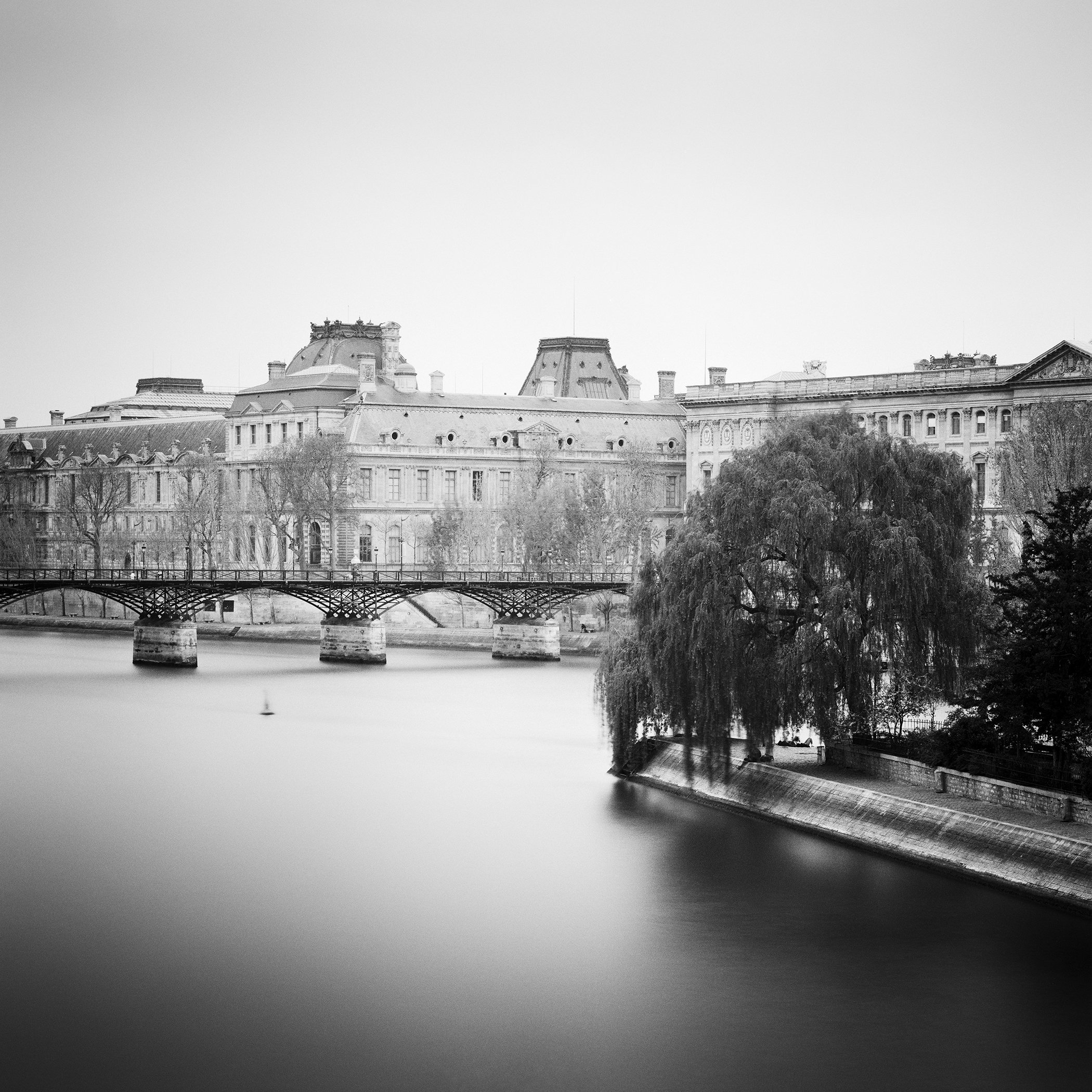 Black-and-white long-exposure photograph of the River Seine, Louvre Palace, a bridge and willow tree in Paris. Photo by Gerald Berghammer.