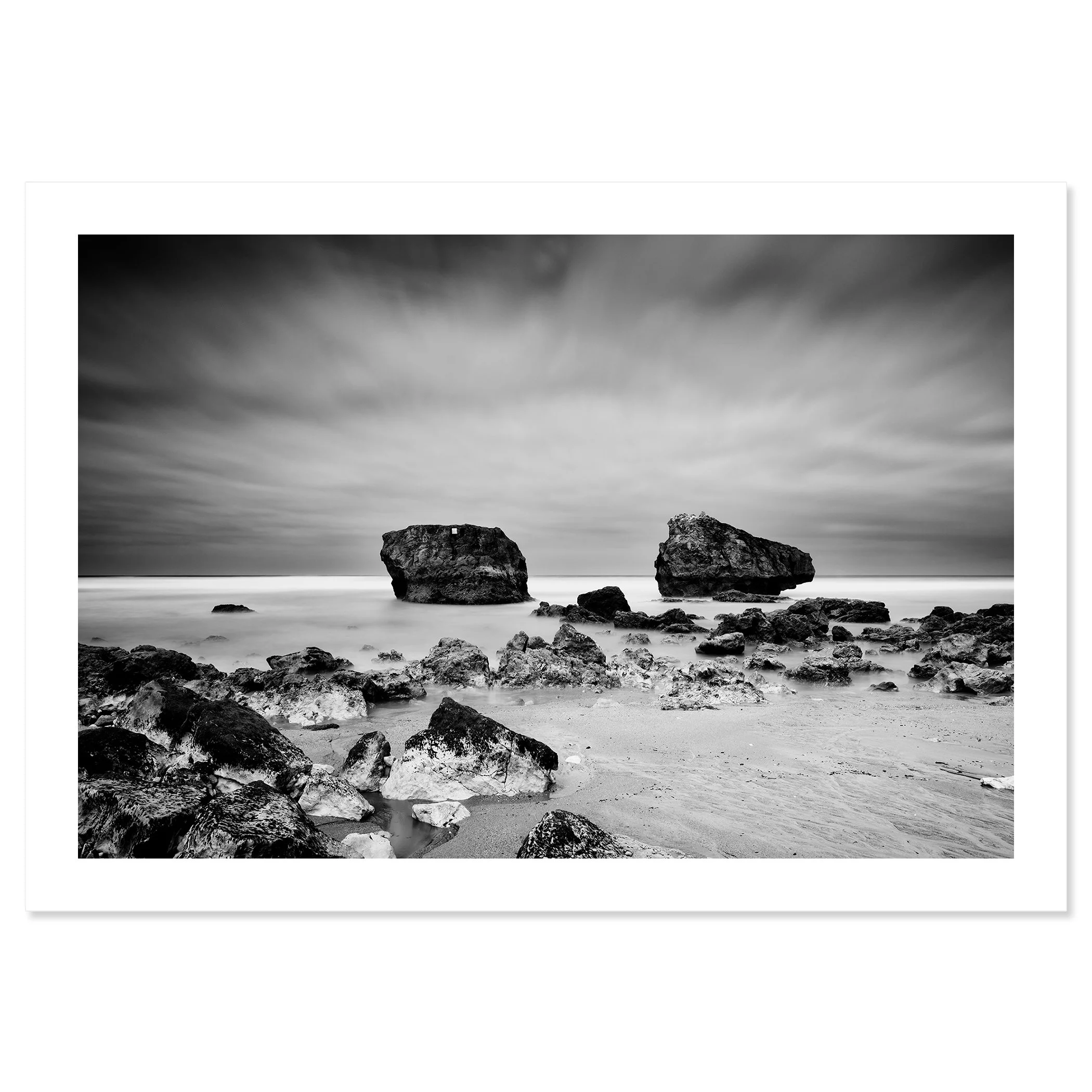 Gerald Berghammer - Black and white landscape photo. Rocky beach with two large rocks protruding from the water, cloudy sky, and smooth ocean surface. Fine art print only