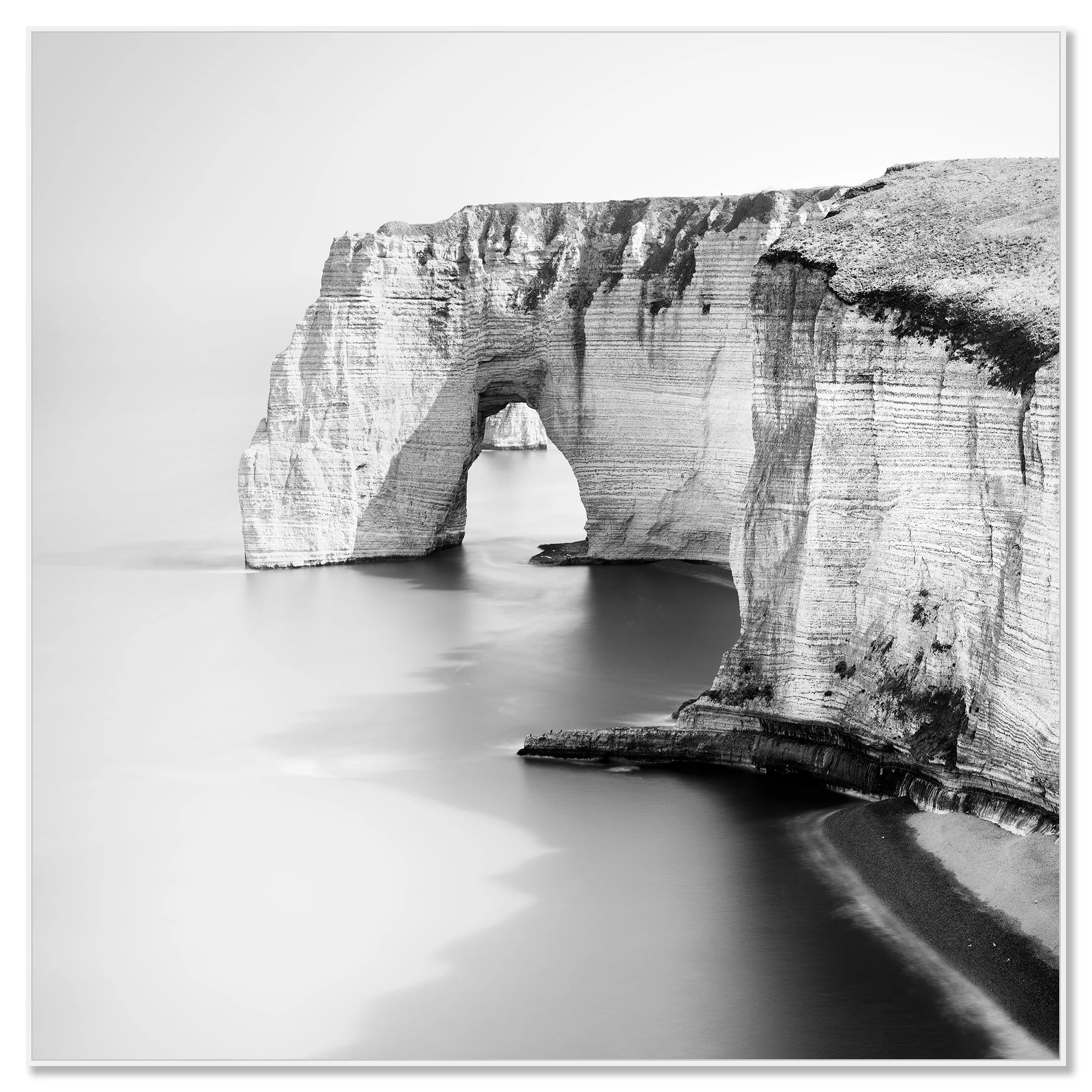 Black and white minimalist seascape photo of a natural rock arch over the water on a rugged coastline – framed ArtBox white