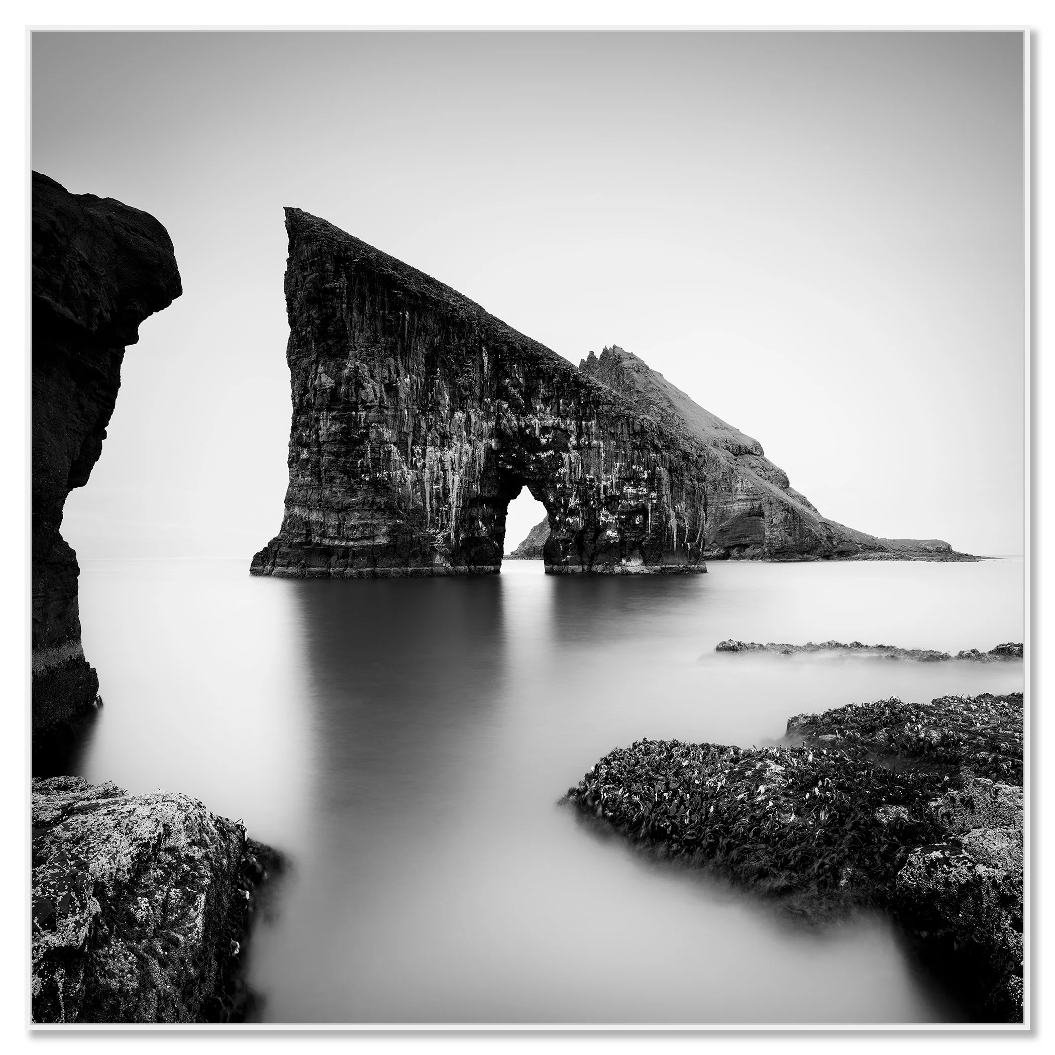 Black and white coastal landscape with a striking sea stack arch and soft long-exposure water – framed ArtBox white