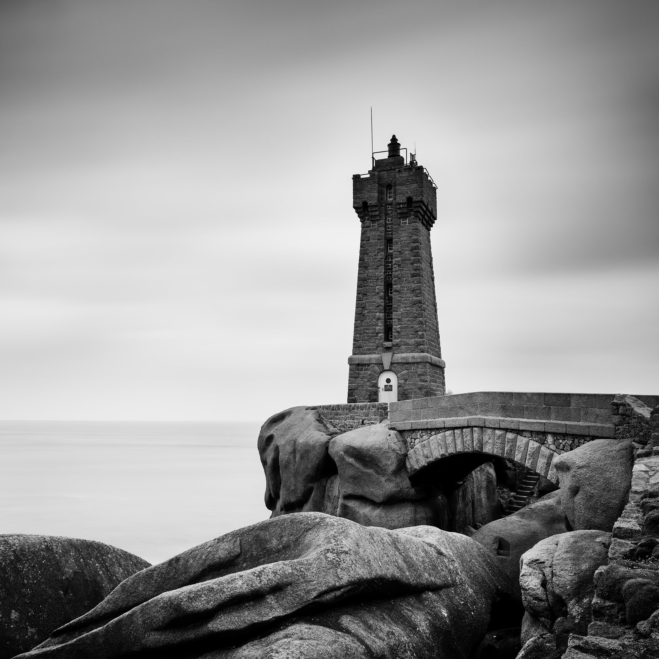 Black-and-white photograph of Ploumanac’h Lighthouse rising above granite rocks on the Brittany coast, France, by Gerald Berghammer.