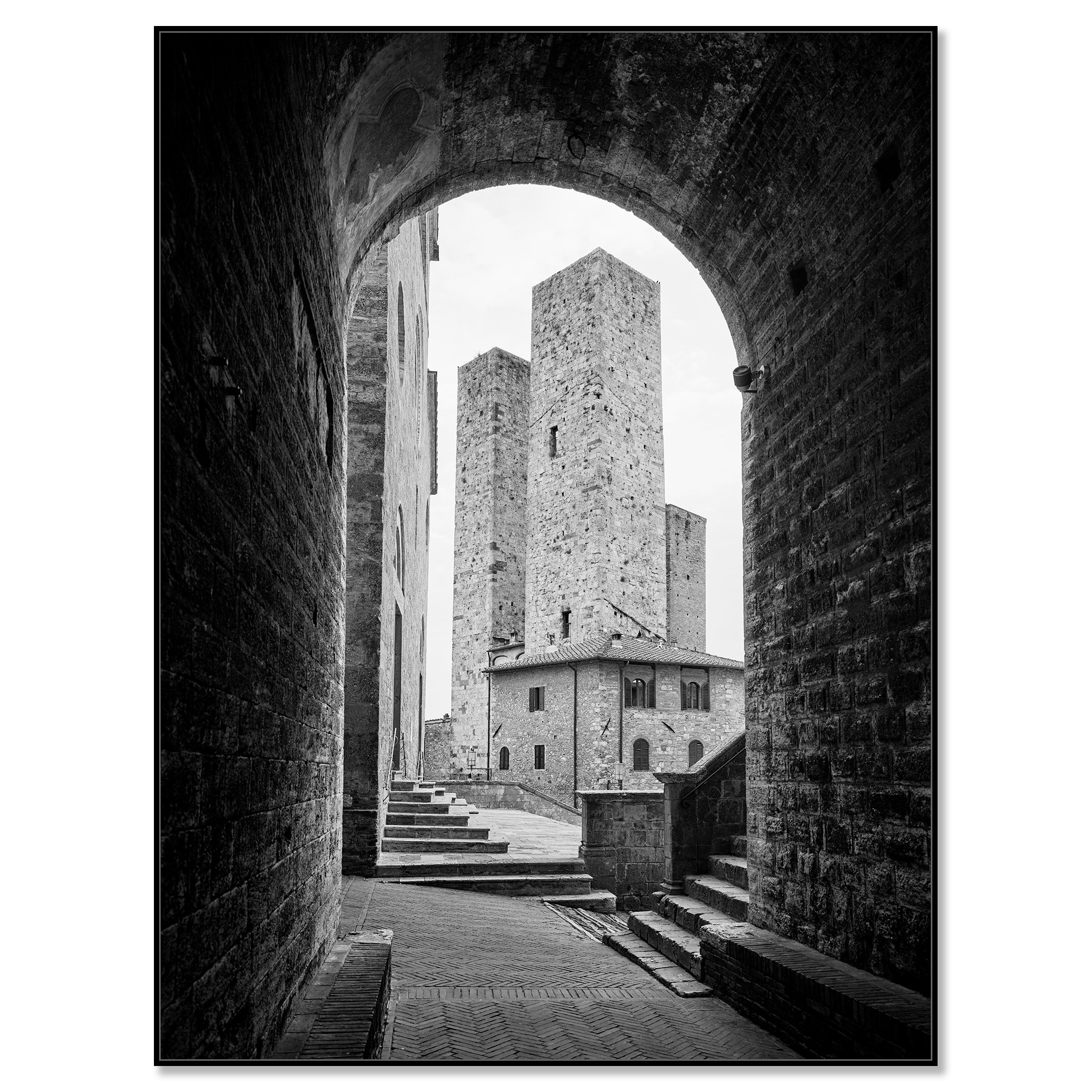 Black-and-white photograph of a medieval stone tower and buildings in San Gimignano, viewed through an arched stone gate – framed ArtBox black