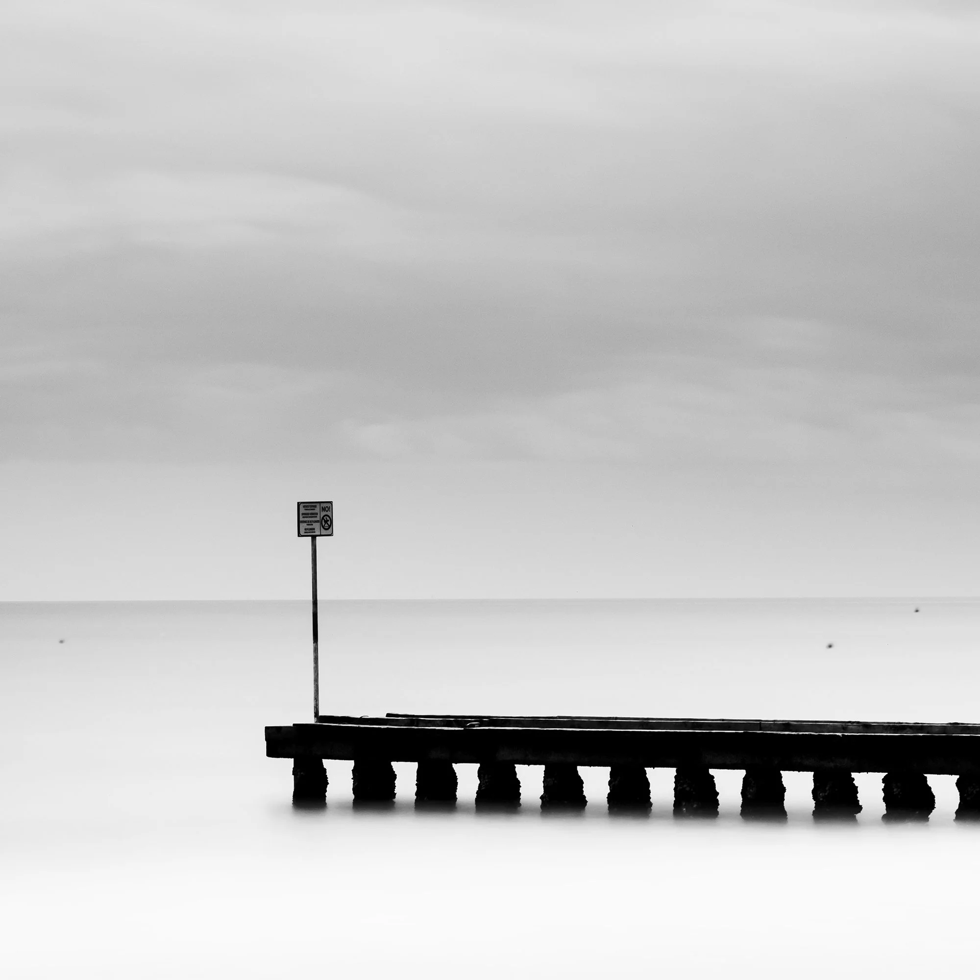 Wooden Pier in the Sea Study 1 – detailed view of the wooden pier extending into a minimalist black-and-white seascape in Italy by Gerald Berghammer.