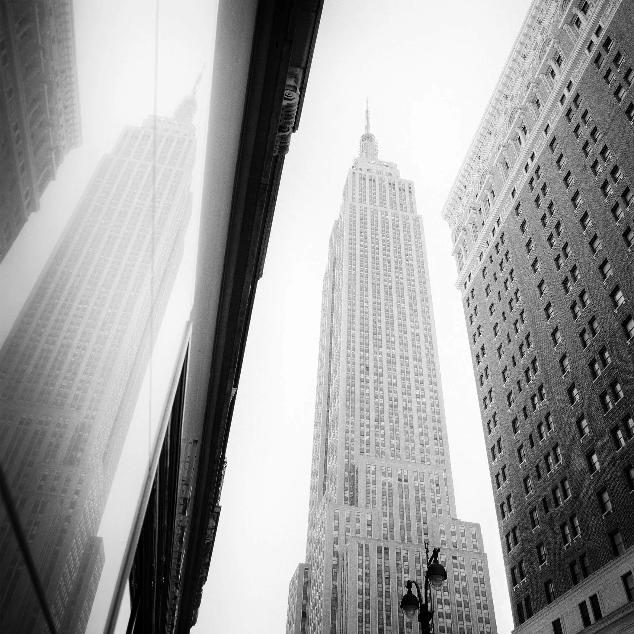 Black-and-white architectural photograph of the Empire State Building and its reflection in New York City by Gerald Berghammer.