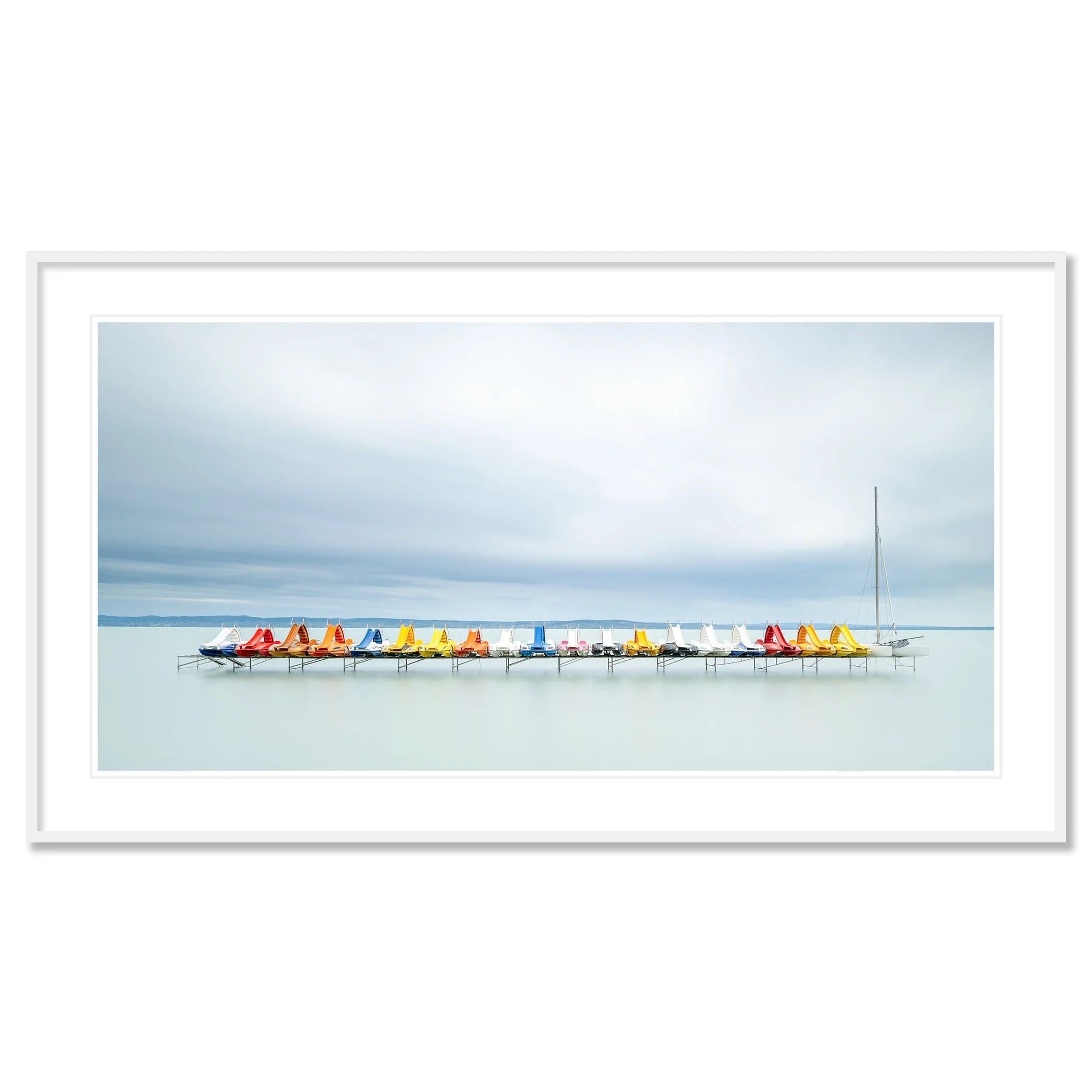 Gerald Berghammer - Color waterscape photography. Colorful pedal boats and a catamaran lined up on a dock on a calm body of water under a cloudy sky. Classic framed white