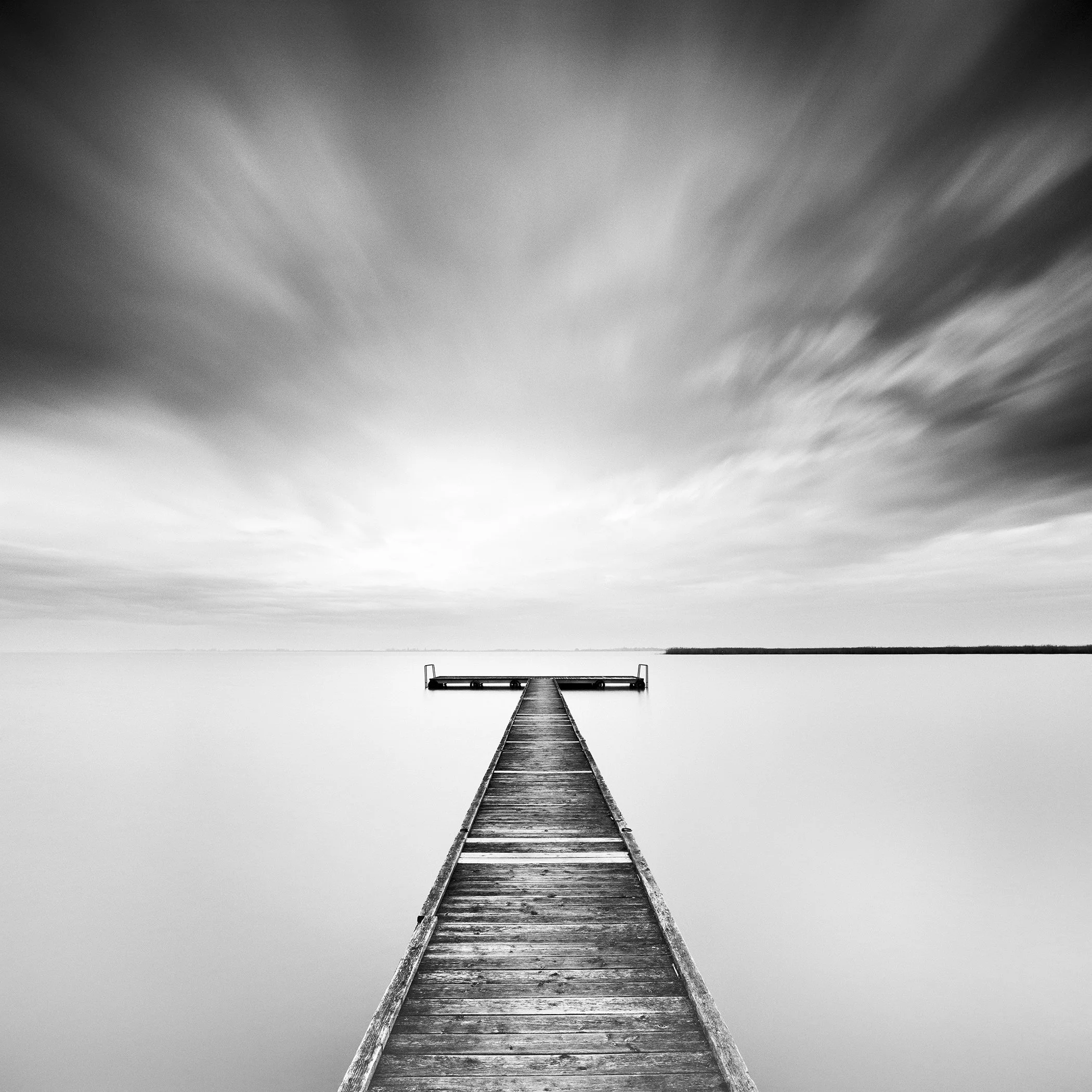 Analogue black-and-white long-exposure photograph of a wooden jetty on Lake Neusiedl beneath storm clouds by Gerald Berghammer.