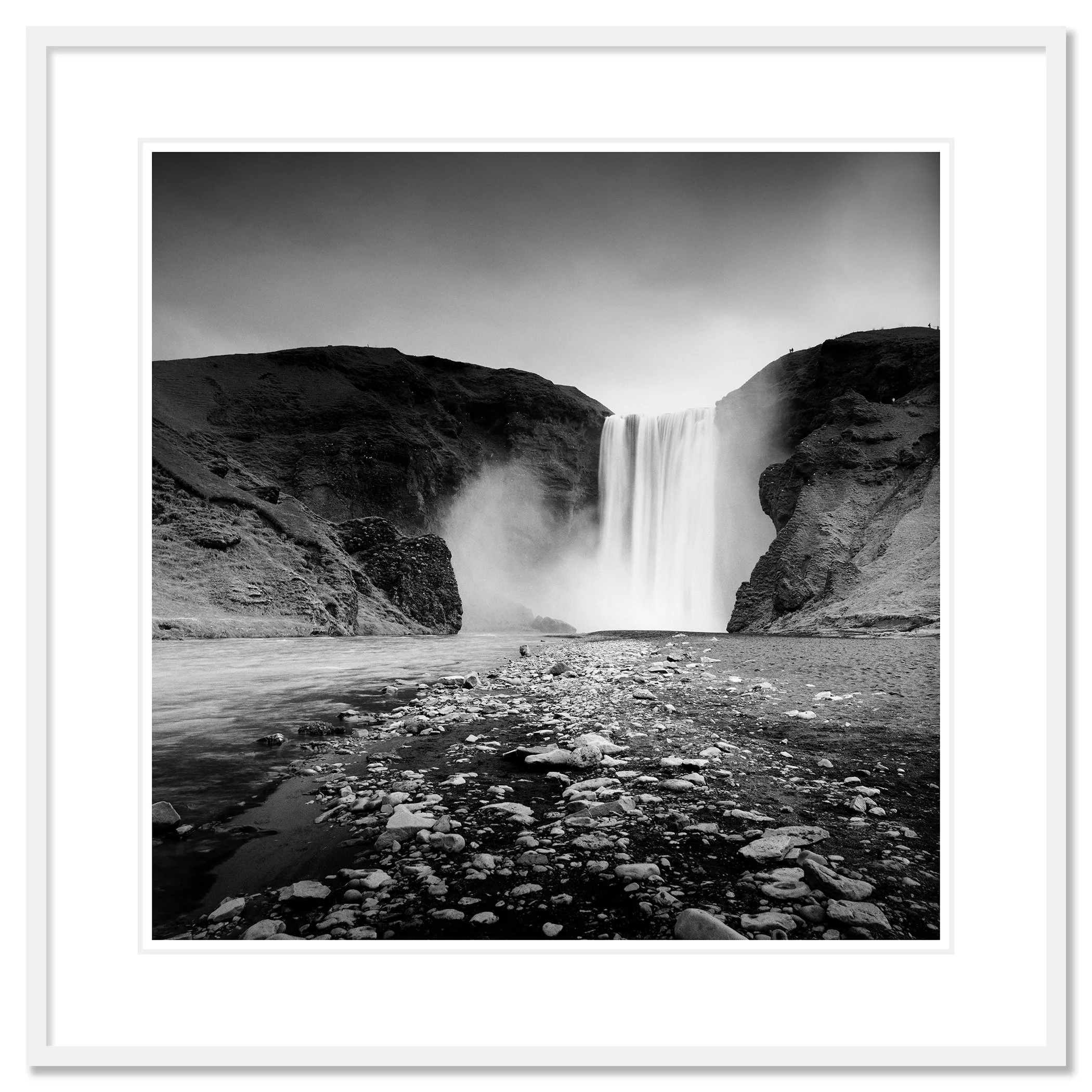 Gerald Berghammer - Black and white long exposure waterscape photography. A large waterfall flowing between rugged cliffs into a rocky river. Classic framed white