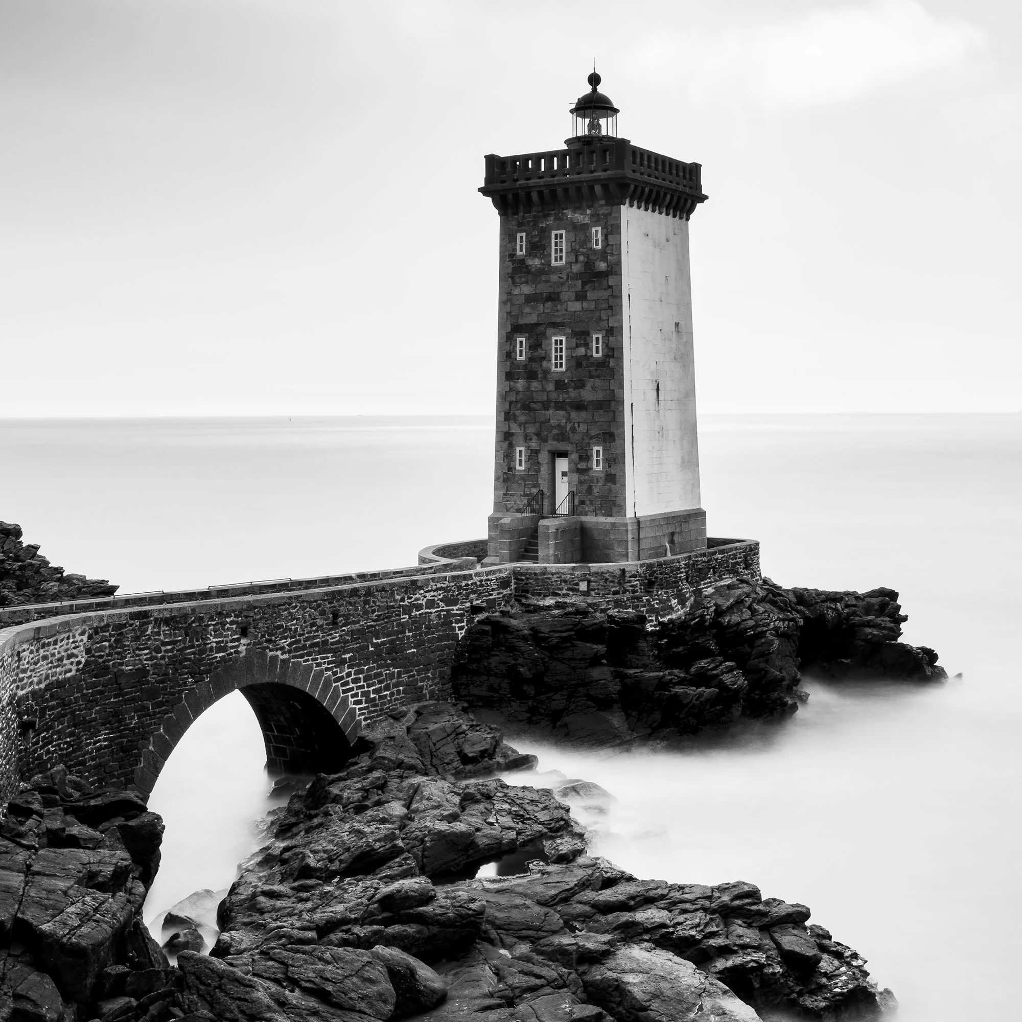 Black-and-white coastal lighthouse with stone bridge across rocks and overcast sky, Detail 3