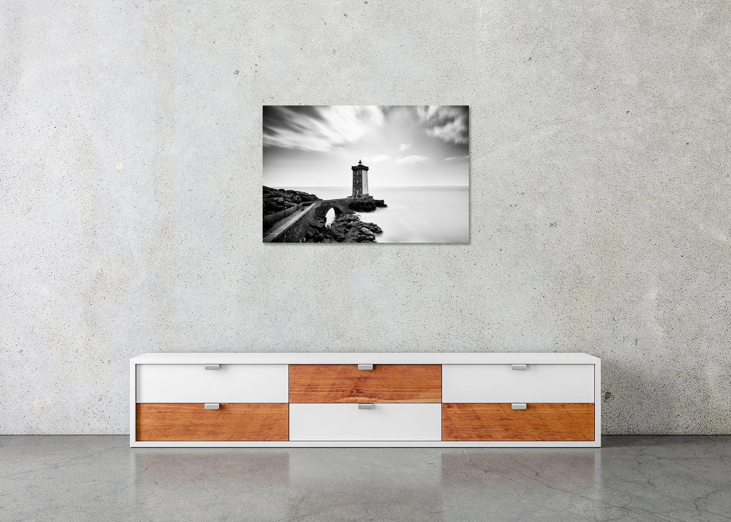 Black and white long-exposure photo of a coastal lighthouse on rocky cliffs, linked by a stone bridge, as a frameless photo print mounted to Dibond.