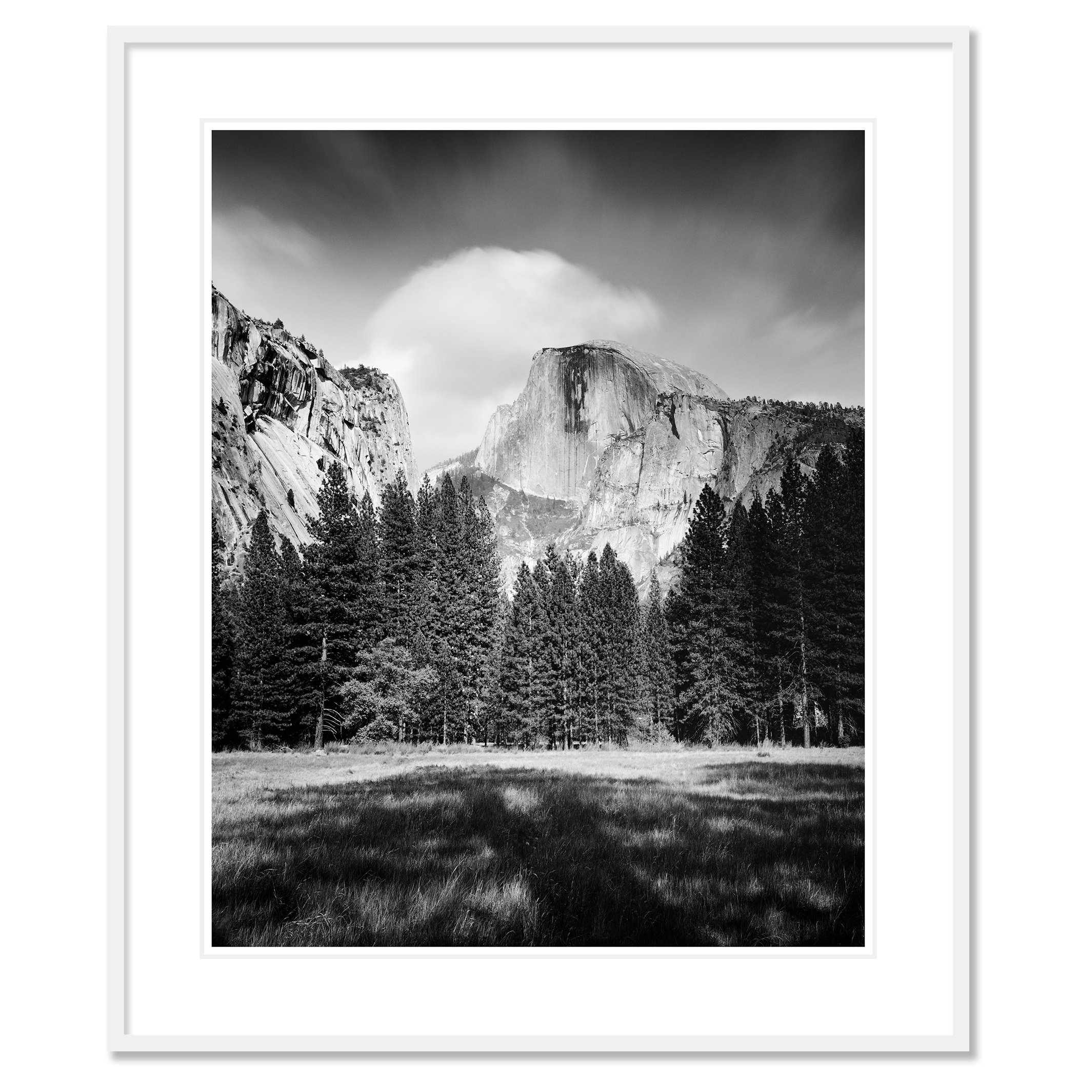 Gerald Berghammer - Black and white Photography. Mountainous landscape with a forest, a large granite rock formation in the background, cloudy sky above. Classic framed white