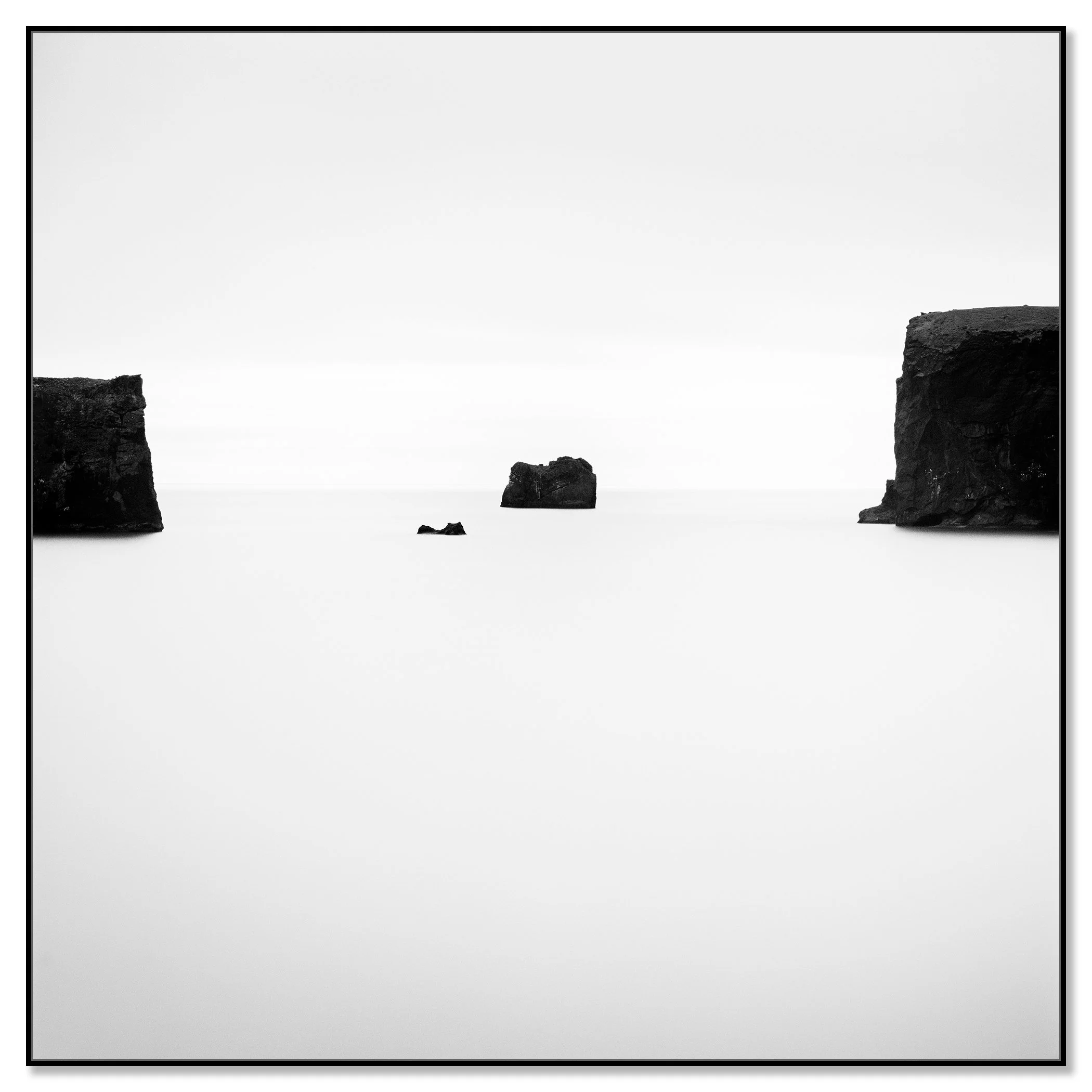 Black and white ocean photo with three rocks emerging from the water: two large rocks at the sides and a smaller rock in the centre – framed ArtBox black