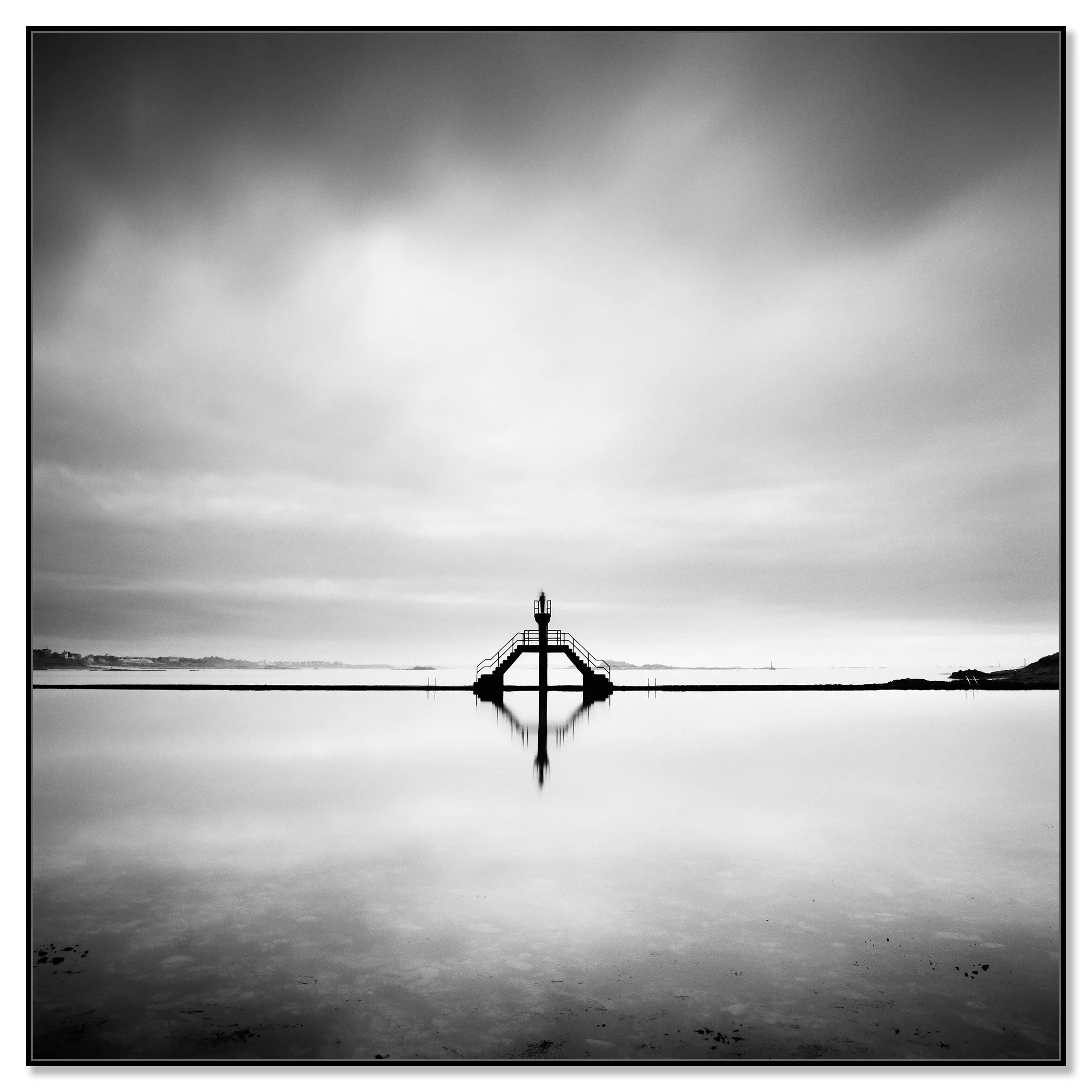Black and white photograph of a small diving platform reflected in calm water under a cloudy sky, minimalist waterscape – framed Artbox black