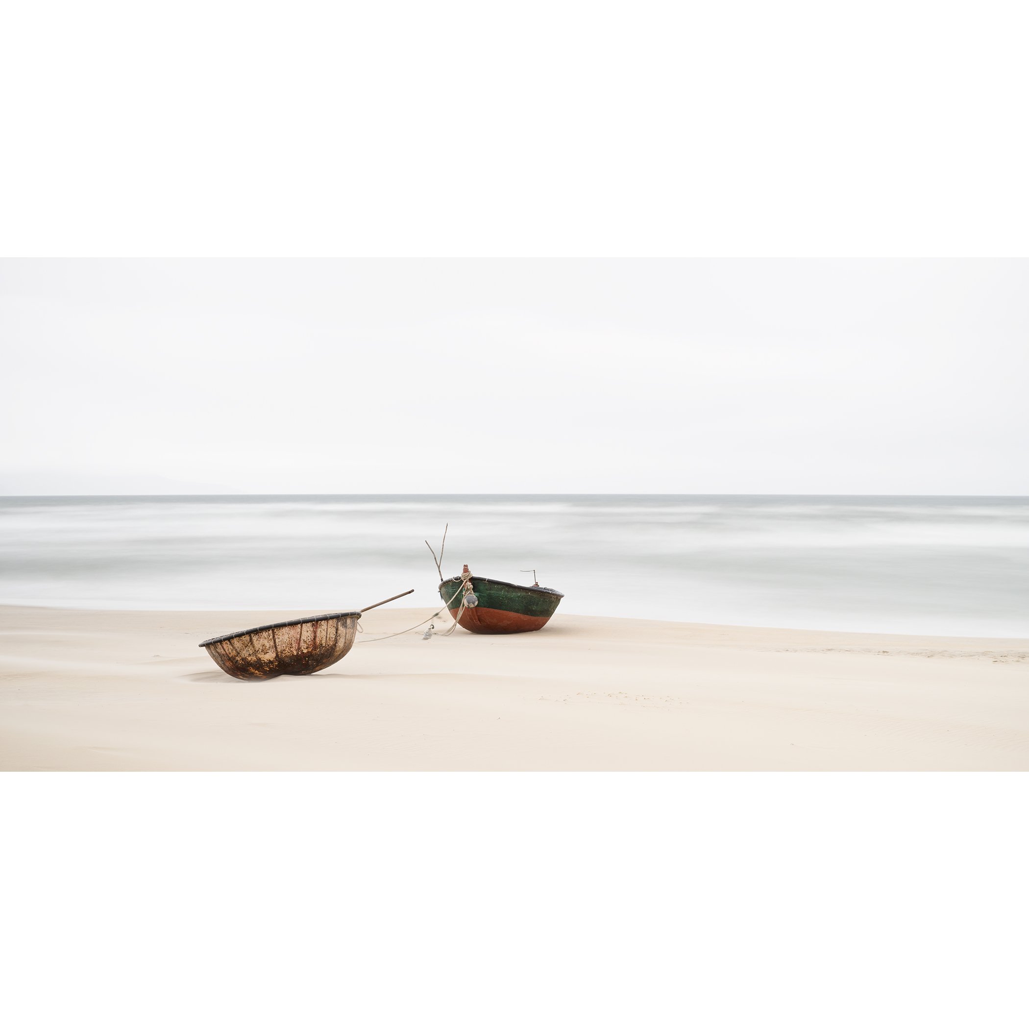 Gerald Berghammer - Color long exposure panorama photography. Two boats resting on a sandy beach near the ocean with calm waves and a cloudy sky.