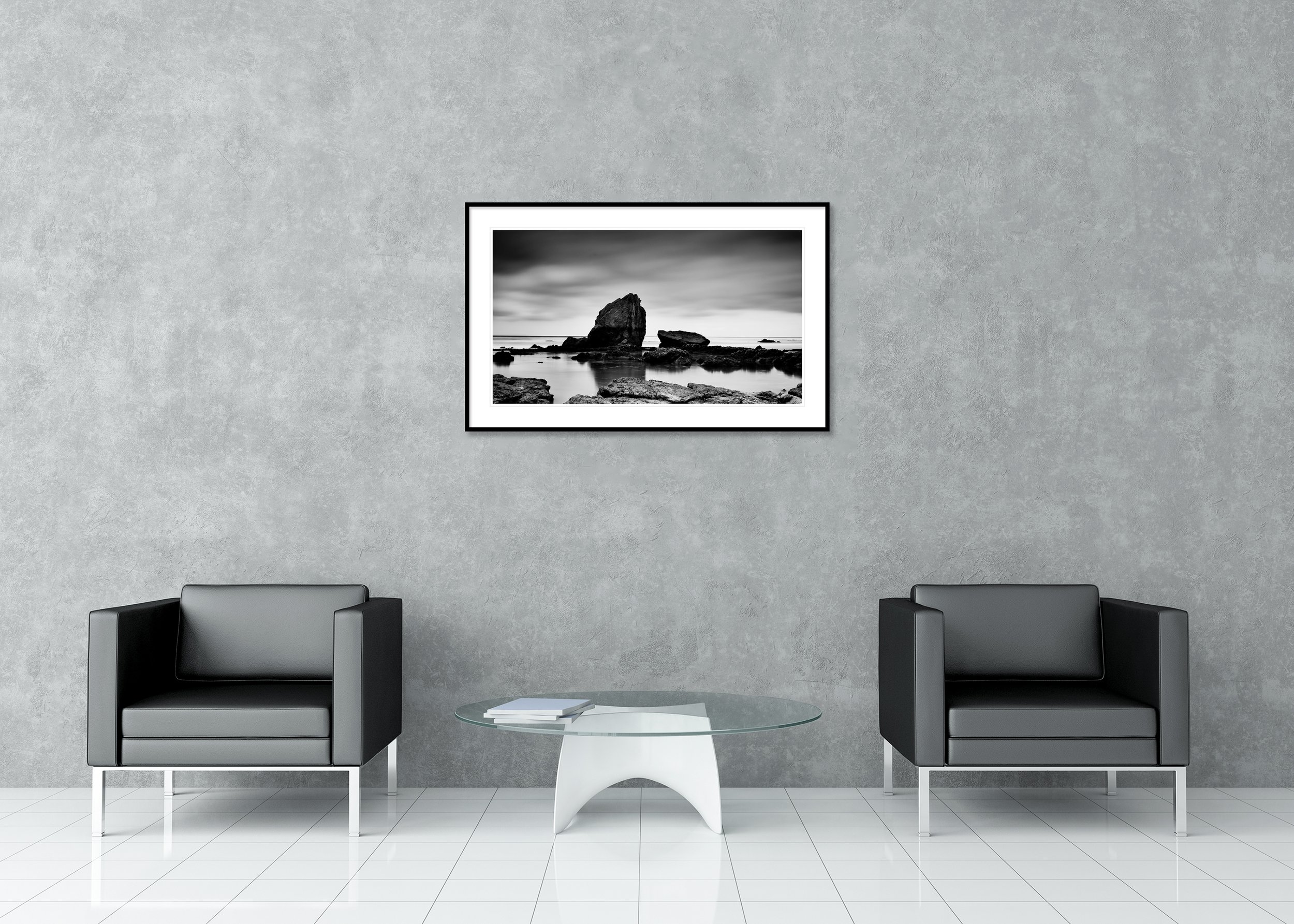 Monochrome coastal landscape print with dramatic sea stack, rocky shoreline and still water at low tide, archival pigment print in a classic frame with mount