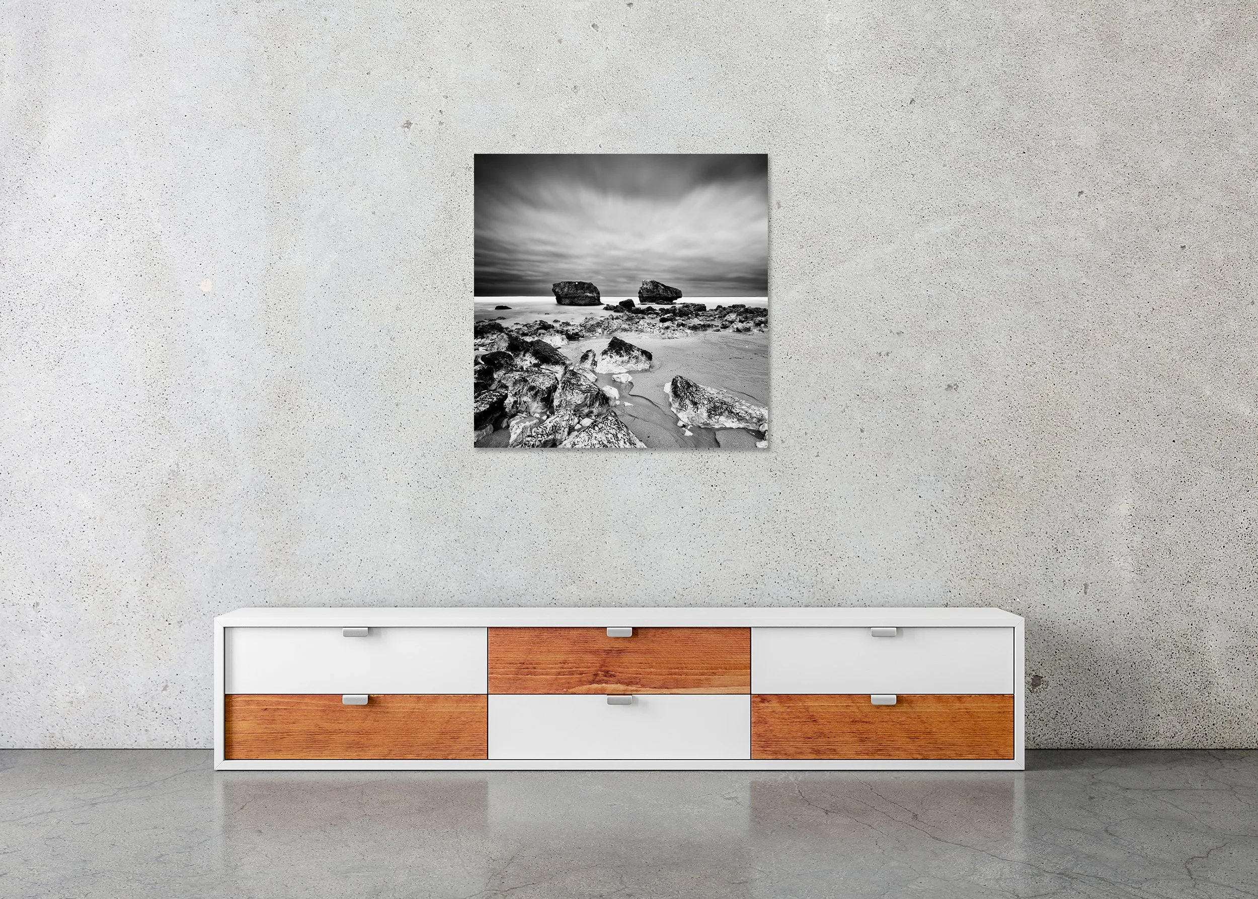Monochrome seascape photo print with stones on sand, two offshore rocks and a moody sky, mounted to Dibond with a frameless finish.