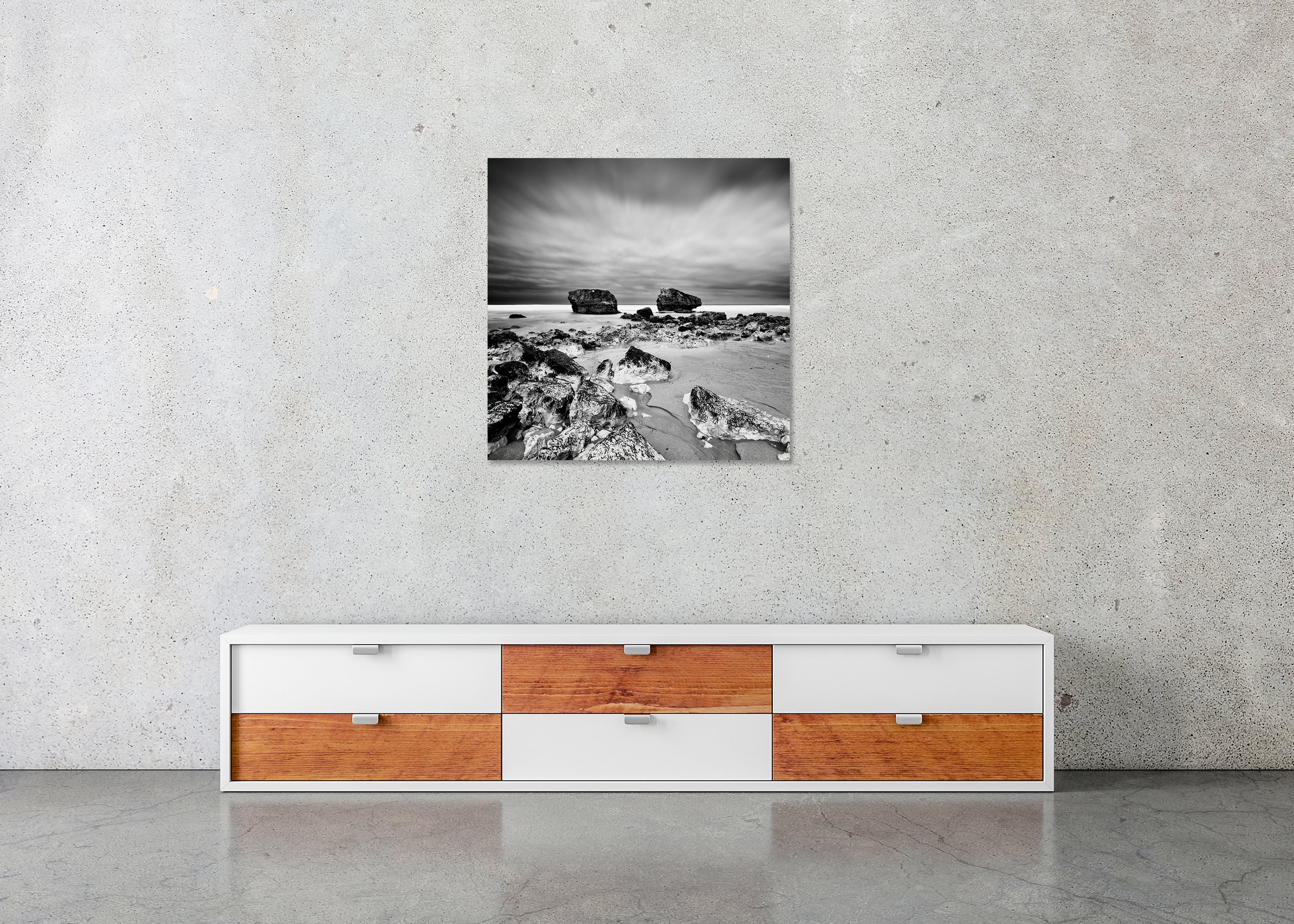 Monochrome seascape with stones on sand, two offshore rocks, and a moody sky, printed on ChromaLuxe metal with a frameless finish.