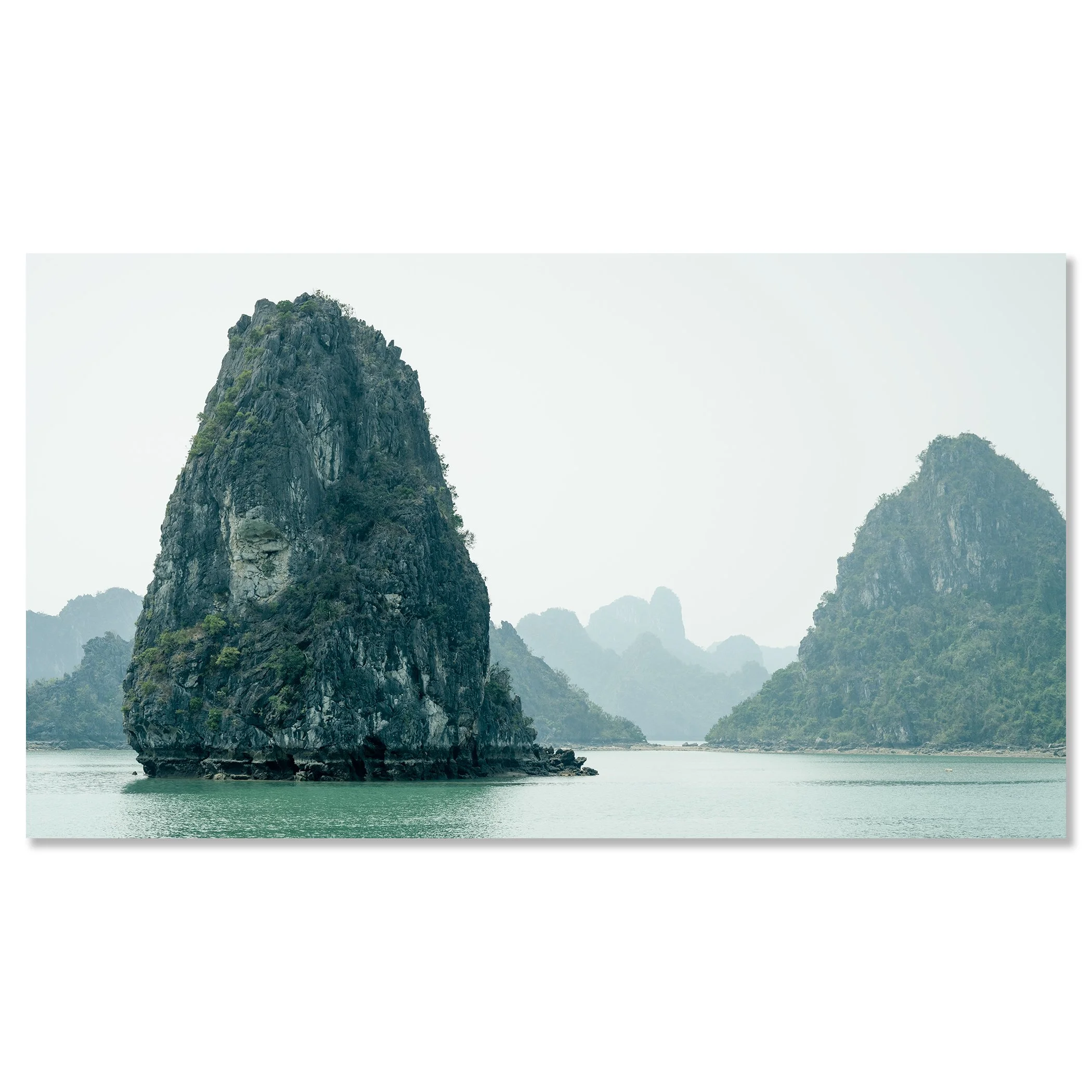 Gerald Berghammer - Color Seascape Photography. Limestone karst formations rise from the water in a tranquil bay, with hazy mountains, Southeast Asia. Chromaluxe frameless