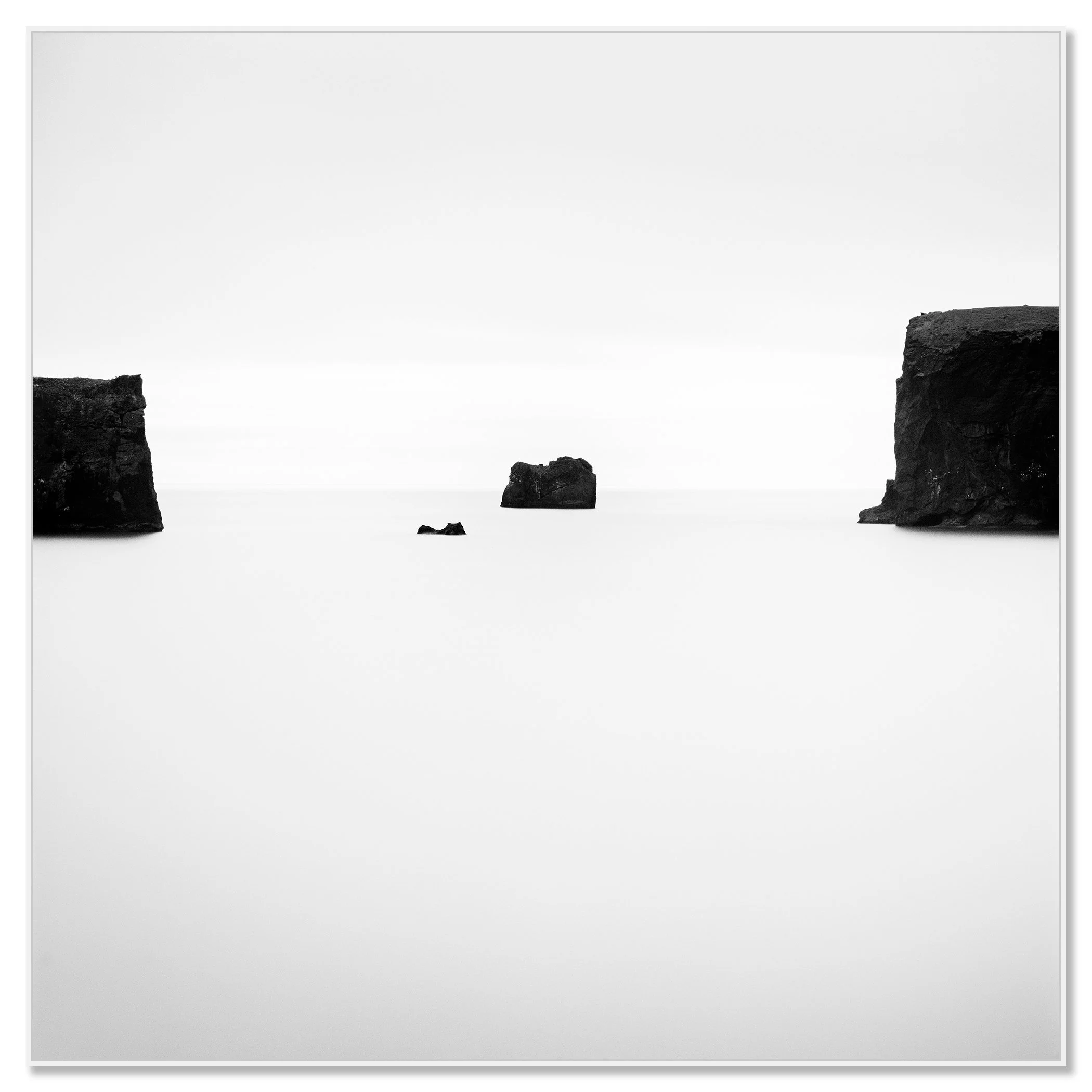 Gerald Berghammer - Black and white photo. Ocean with three rocks protruding from water, two large rocks on either side and a smaller rock in the middle. Chromaluxe framed white