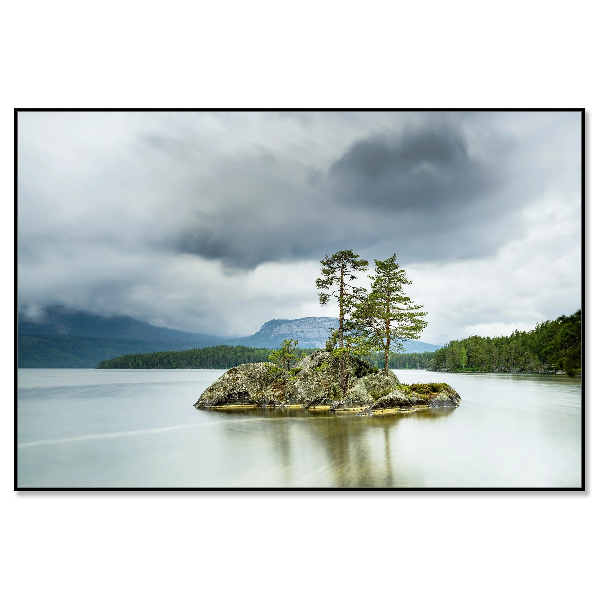 Gerald Berghammer - Color Photography. A small rocky island with tall pine trees surrounded by a calm lake under a cloudy sky and mountains behind. Chromaluxe framed black