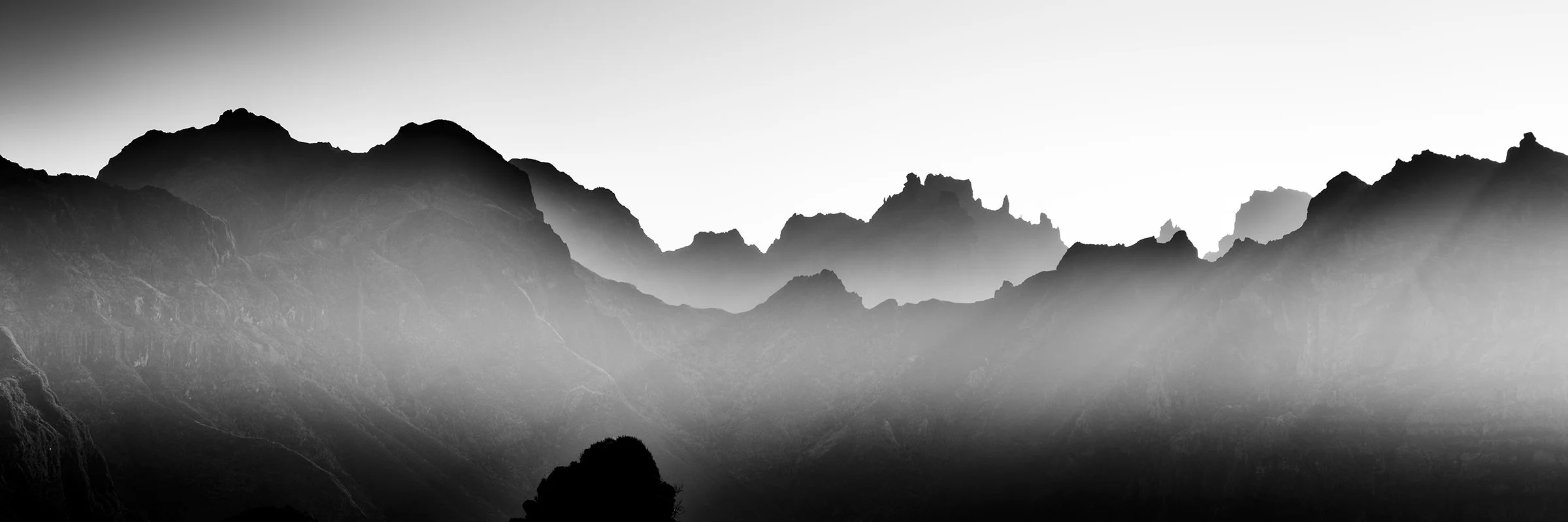 Panoramic black-and-white fine art photograph of rugged mountain ridges emerging through mist in Madeira, Portugal, by Gerald Berghammer.