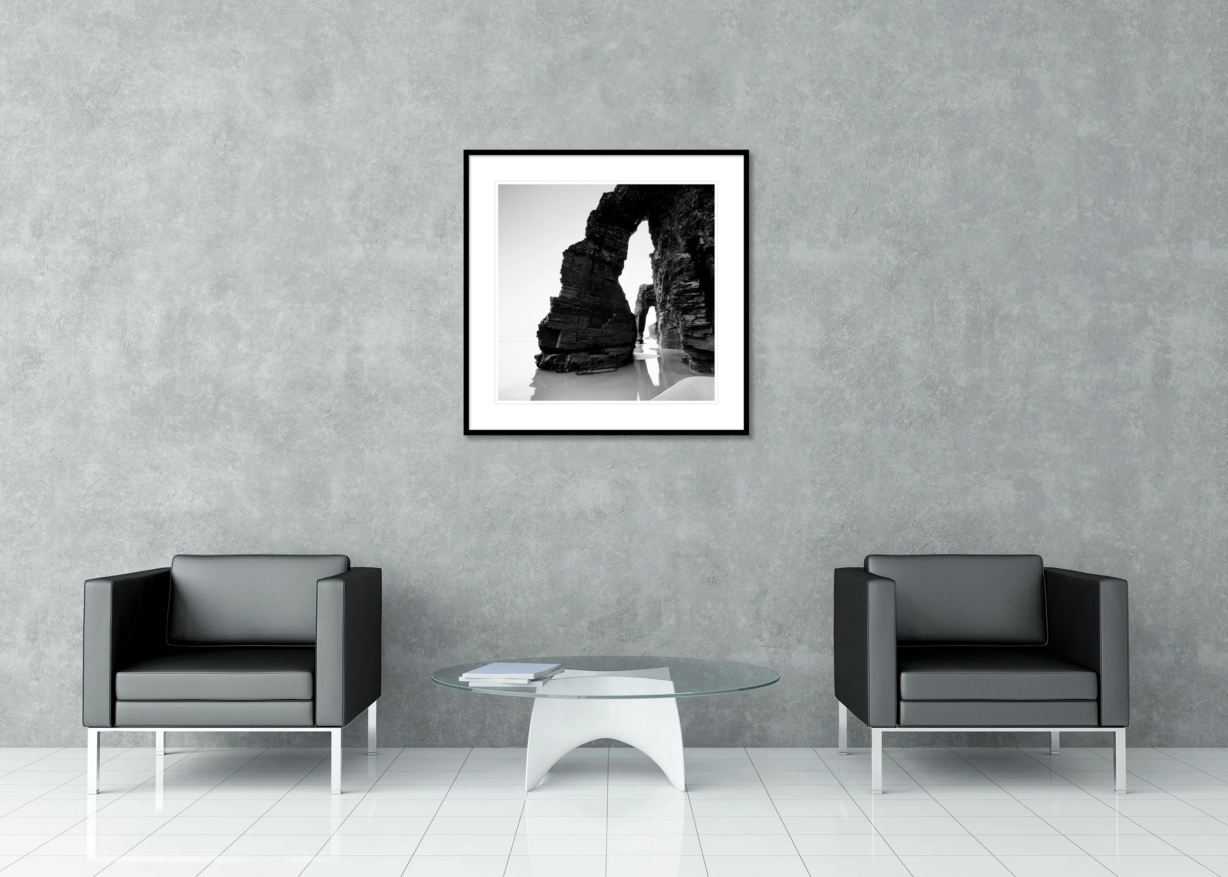 Black and white coastal photo of rugged cliffs and sea arches reflected in wet sand, archival pigment print in a classic frame with a mount
