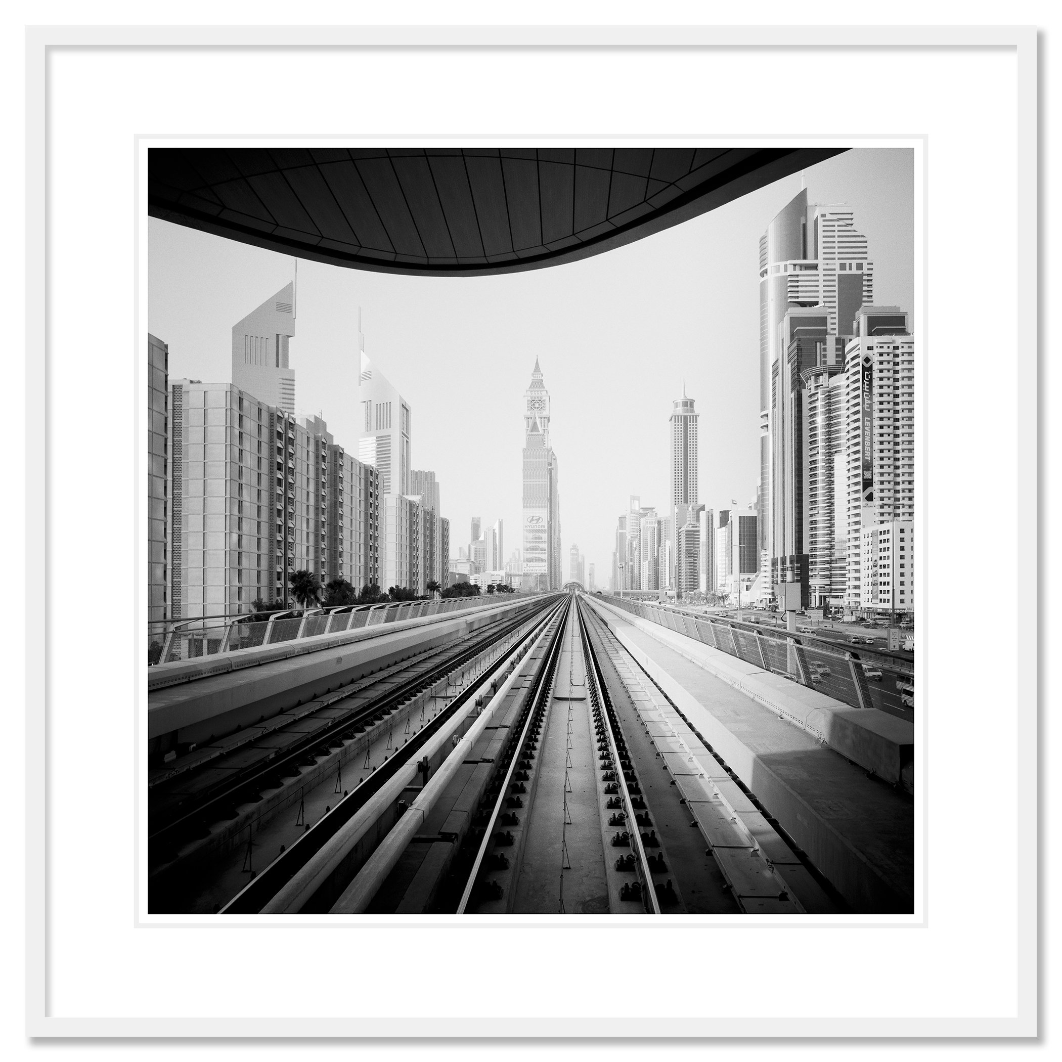 Gerald Berghammer - Black and white cityscape photo. City skyline viewed from a railway track, with modern skyscrapers and a clock tower in the distance. Classic framed white