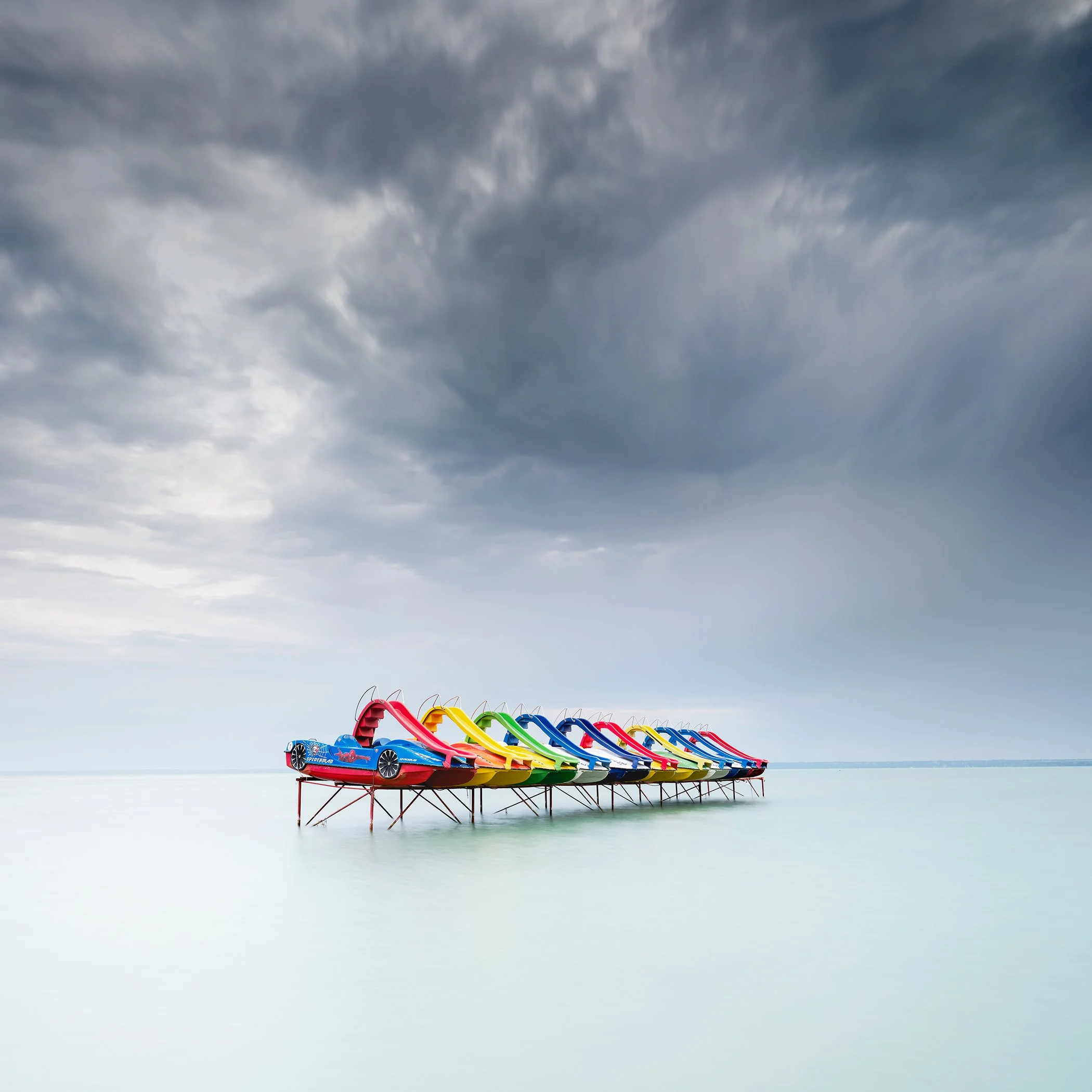 Colourful pedal boats beneath dramatic storm clouds on the calm waters of Lake Balaton, Hungary. Photo by Gerald Berghammer.