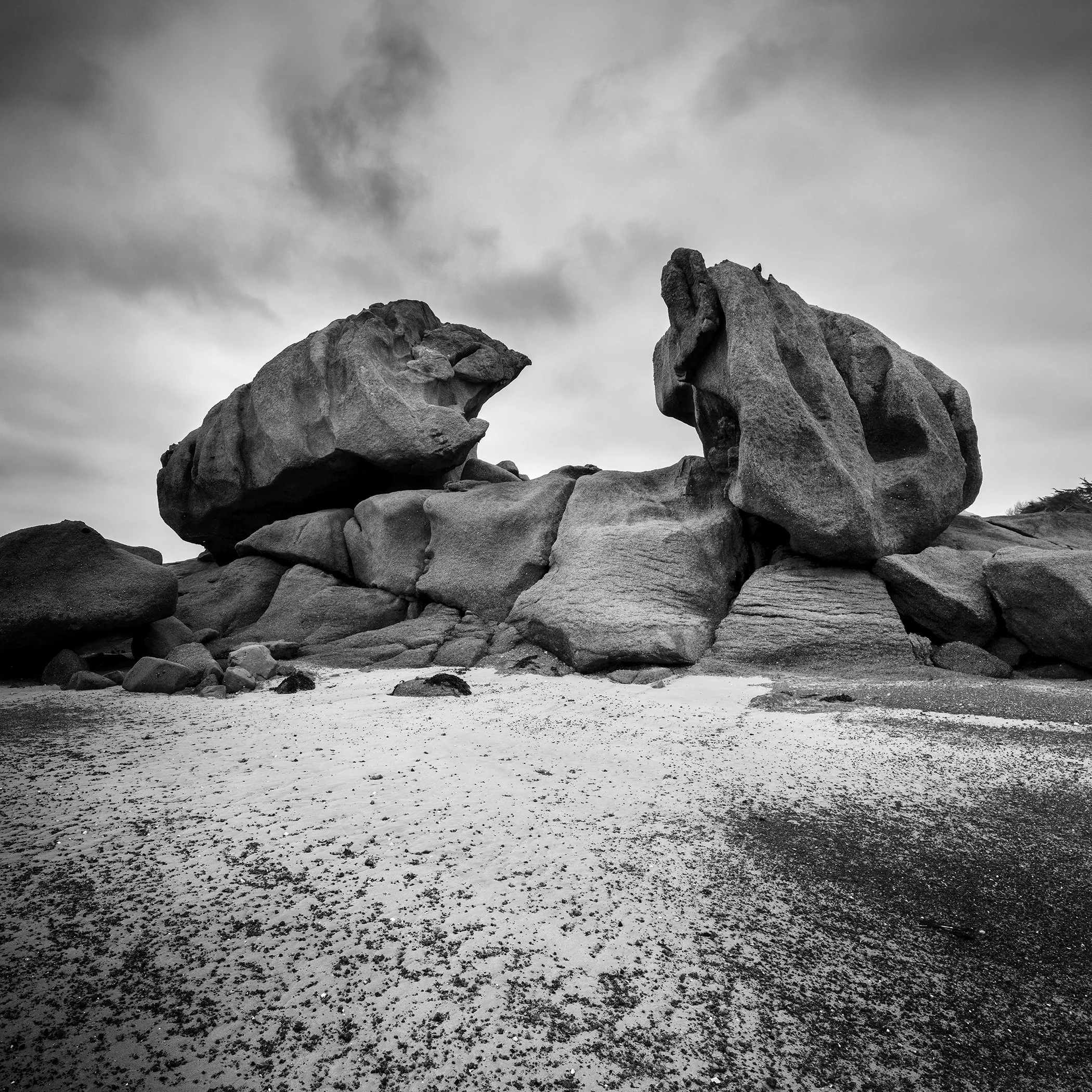 Black and white photo of massive granite rock formations on a sandy granit coast under a dramatic cloudy sky