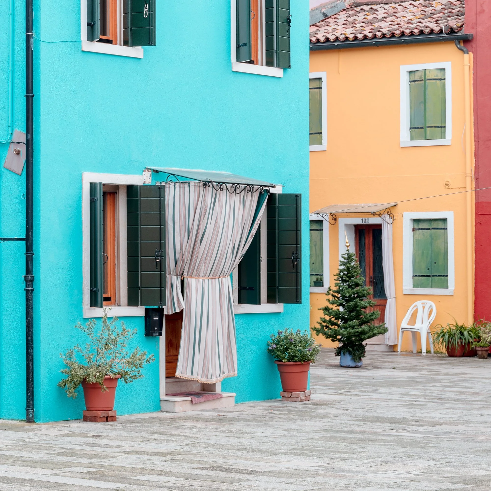 © 2025 Gerald Berghammer - Color cityscape photography. Colorful buildings with pastel pink, blue, yellow, and red walls, windows, and open shutters in a courtyard. Print detail 3
