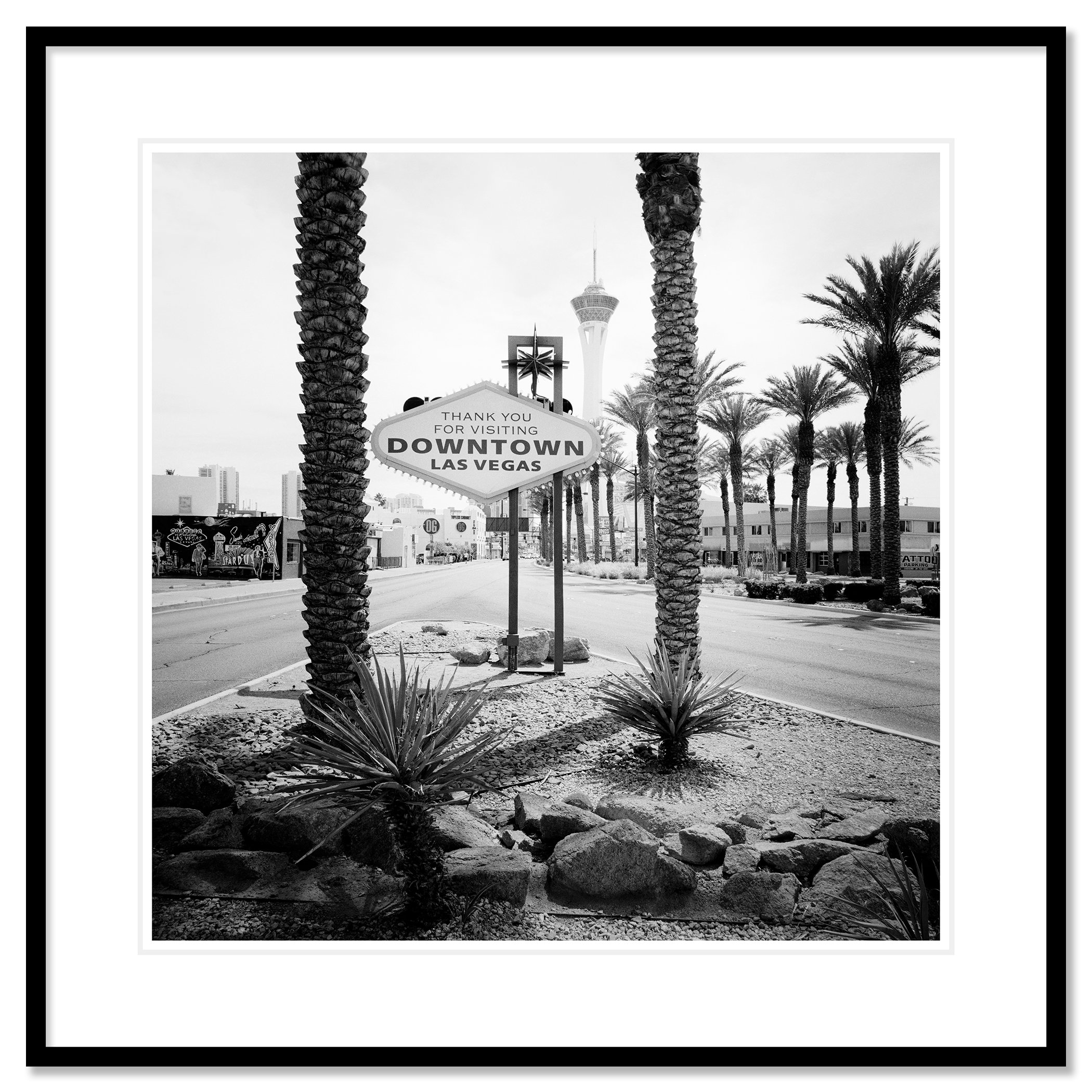 Gerald Berghammer - Black and white desert cityscape photography. Las Vegas Welcome Sign, with palm trees lining the street and the Stratosphere Tower. Classic framed black
