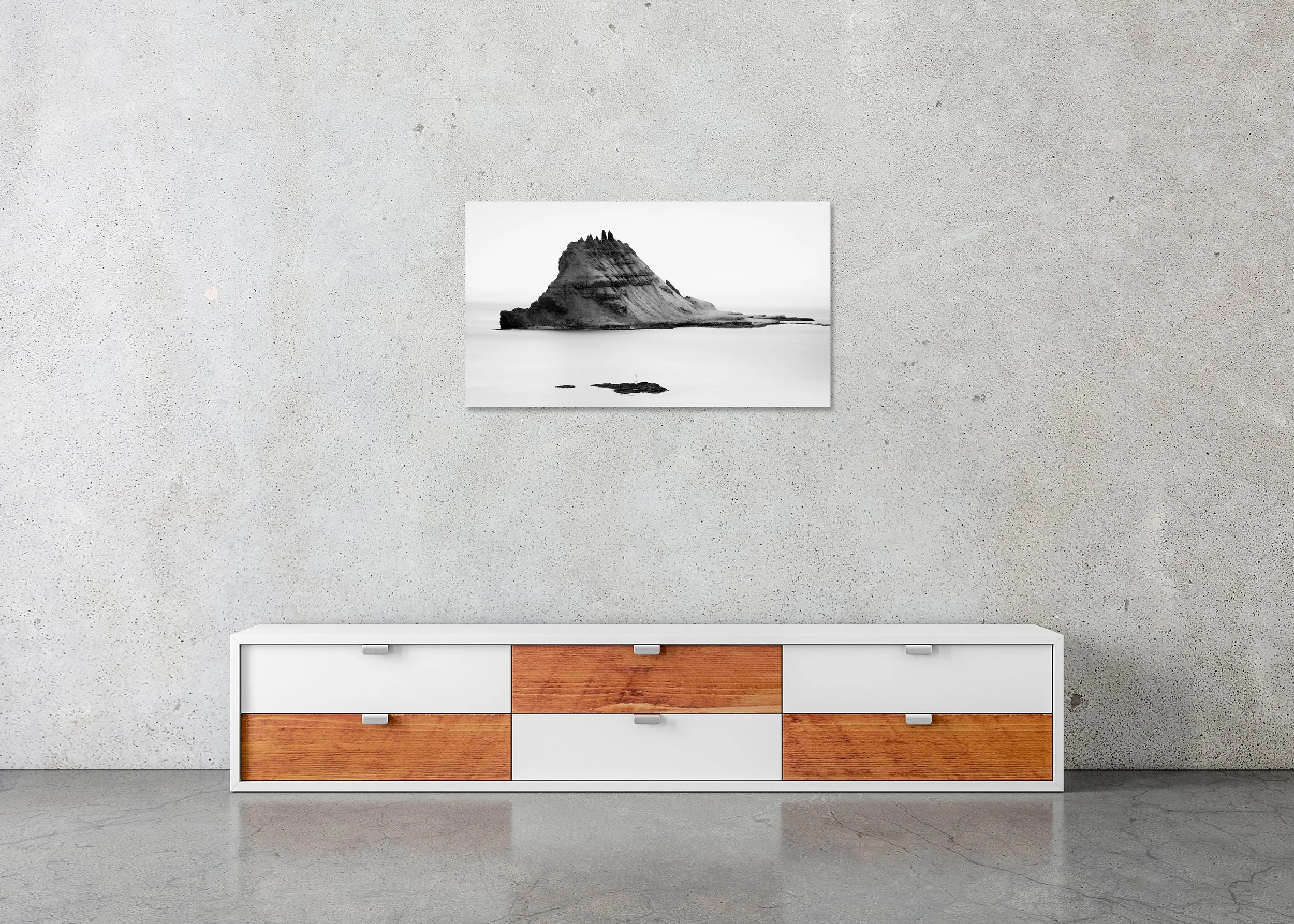 Black and white long-exposure photograph of a rugged rocky island rising from a calm sea beneath a minimalist sky, mounted to Dibond, frameless.