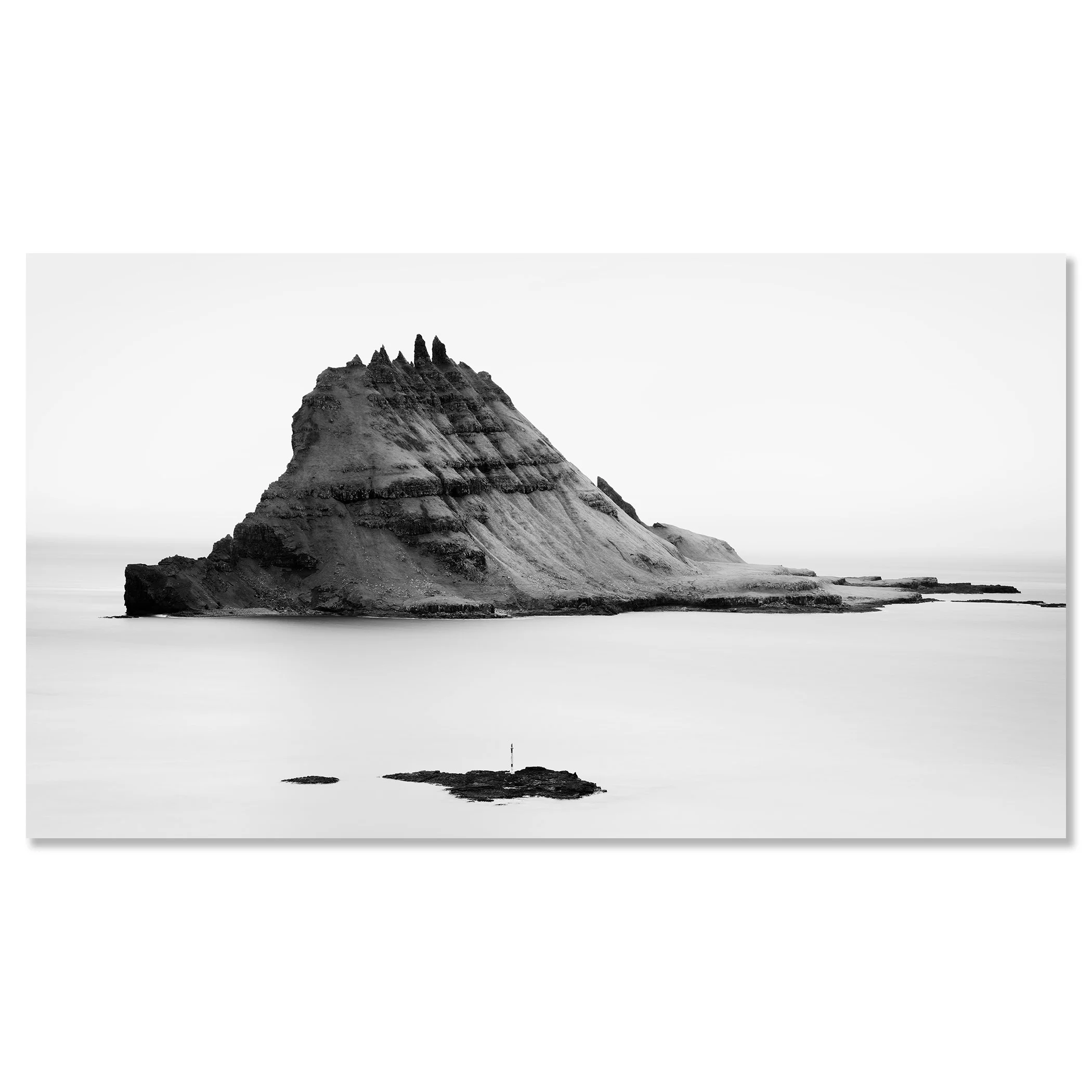 Black-and-white panoramic photo of a layered sea stack in the ocean, with smaller rocks in the foreground and waves – dibond frameless