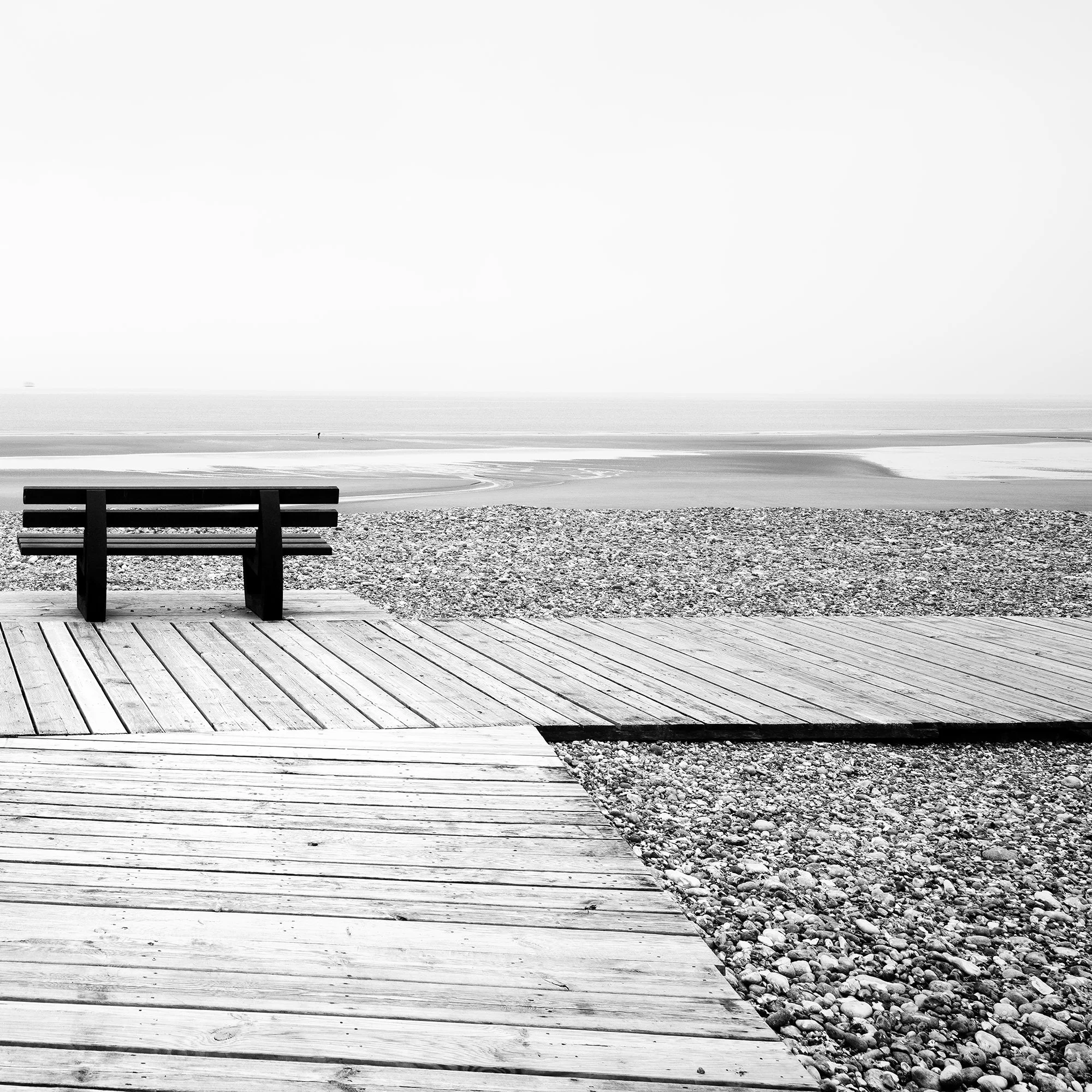 Detail of Relaxing Point Study 1 by Gerald Berghammer, showing the solitary bench, pebble beach and calm sea in France.