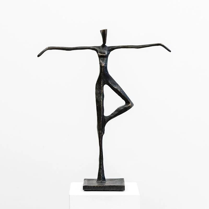Abstract metal sculpture of a human figure in a yoga pose, balancing on one leg with arms extended sideways.