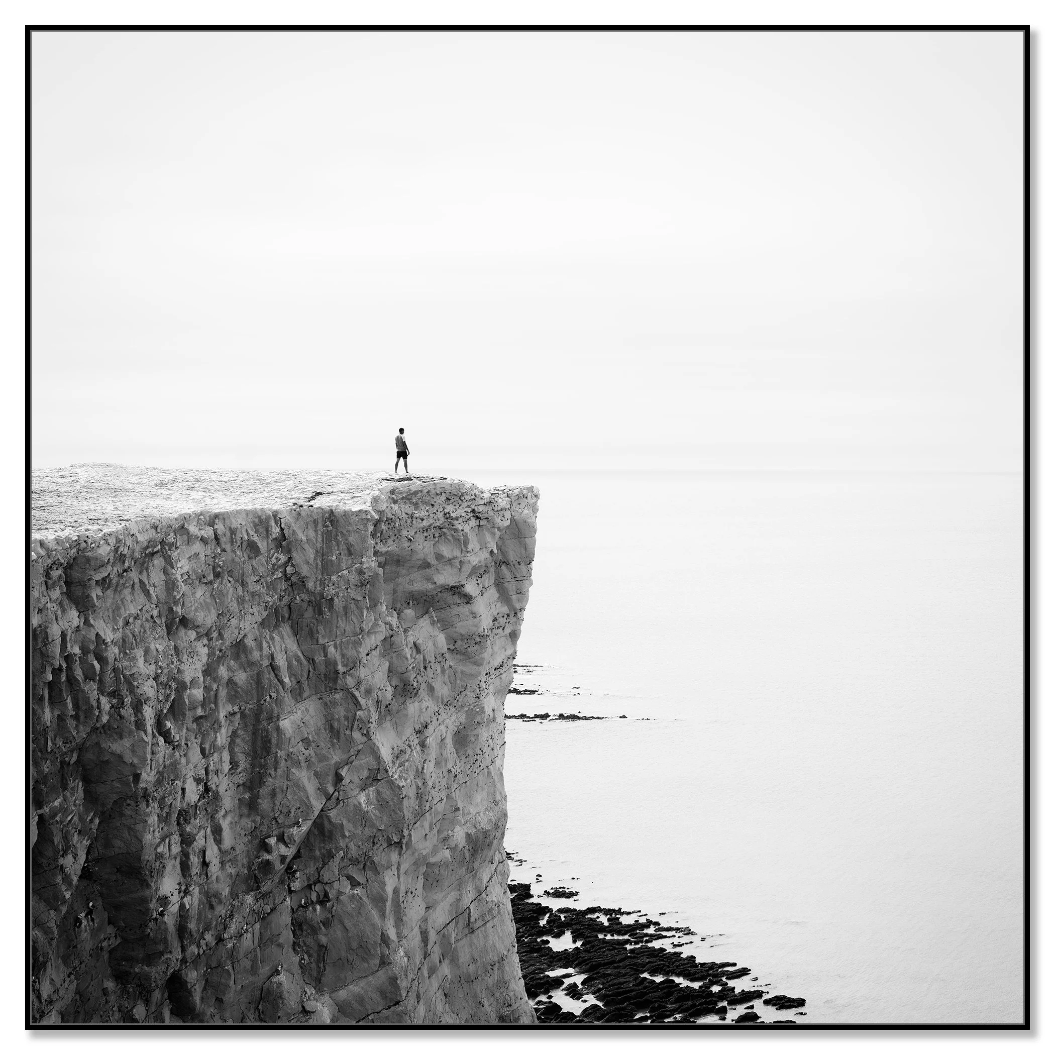 Person standing alone on a white cliff edge overlooking the England coast and ocean – framed ArtBox black