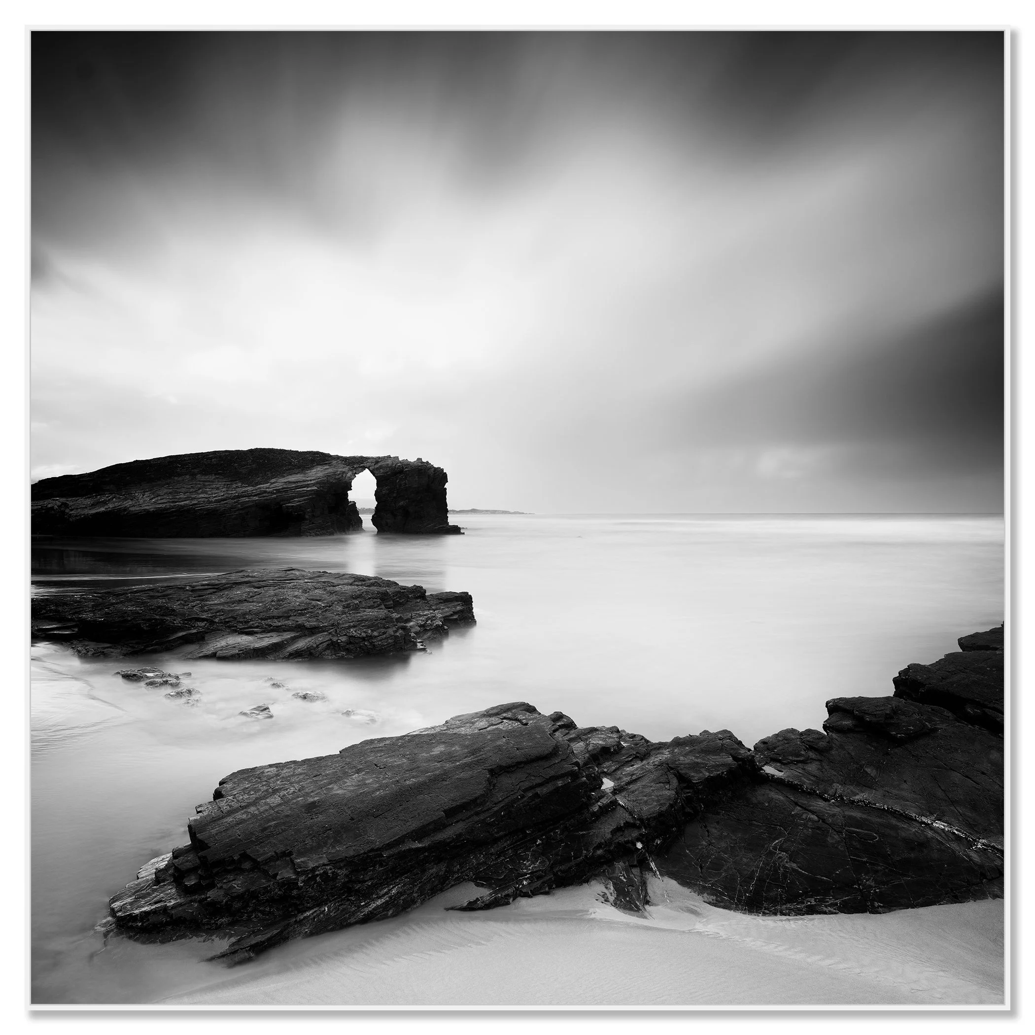 As Catedrais Beach rock arch in black-and-white, rocky shoreline and calm sea under a cloudy sky – framed ArtBox white