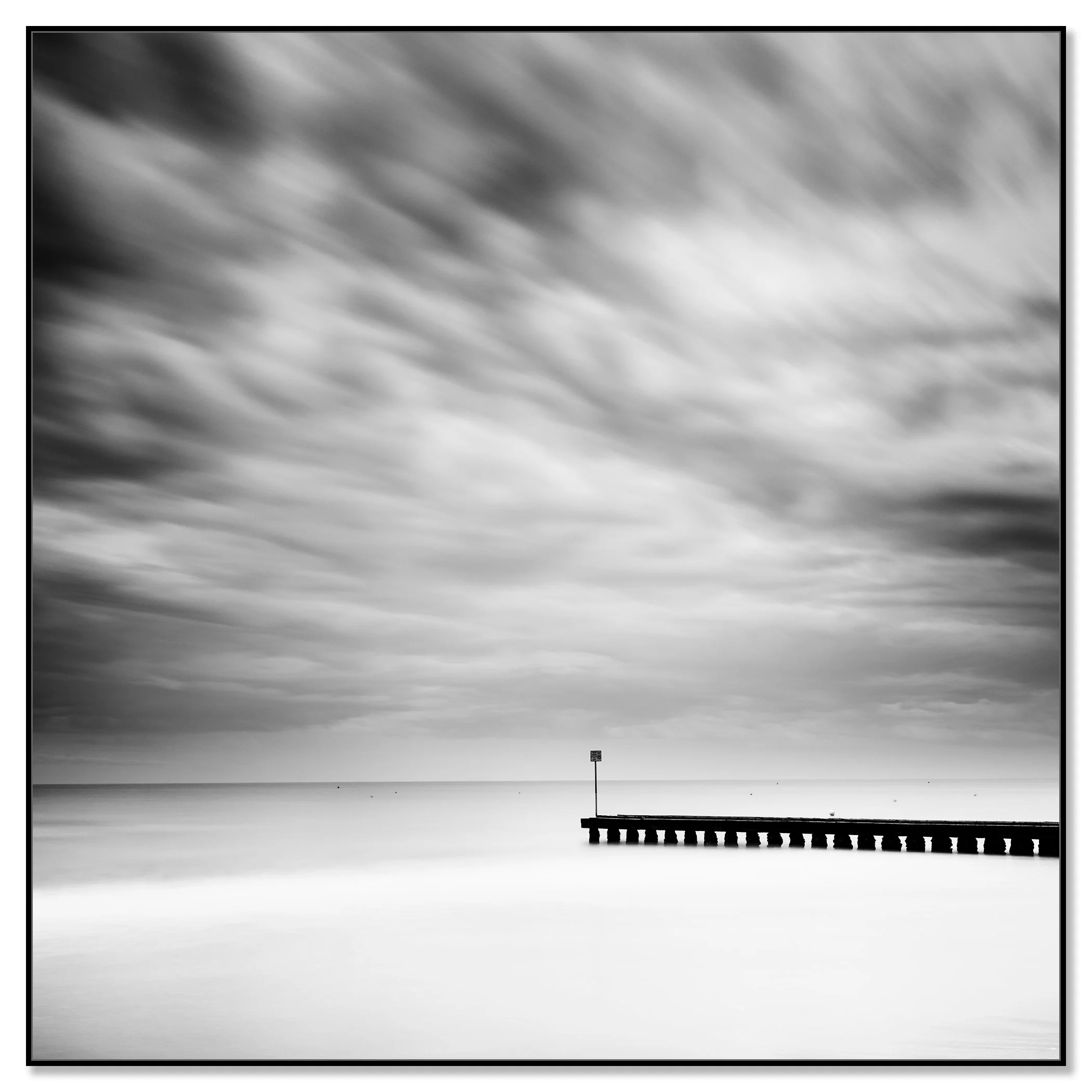 Fine art black and white seascape with moving clouds and a pier reaching towards the horizon – framed ArtBox black