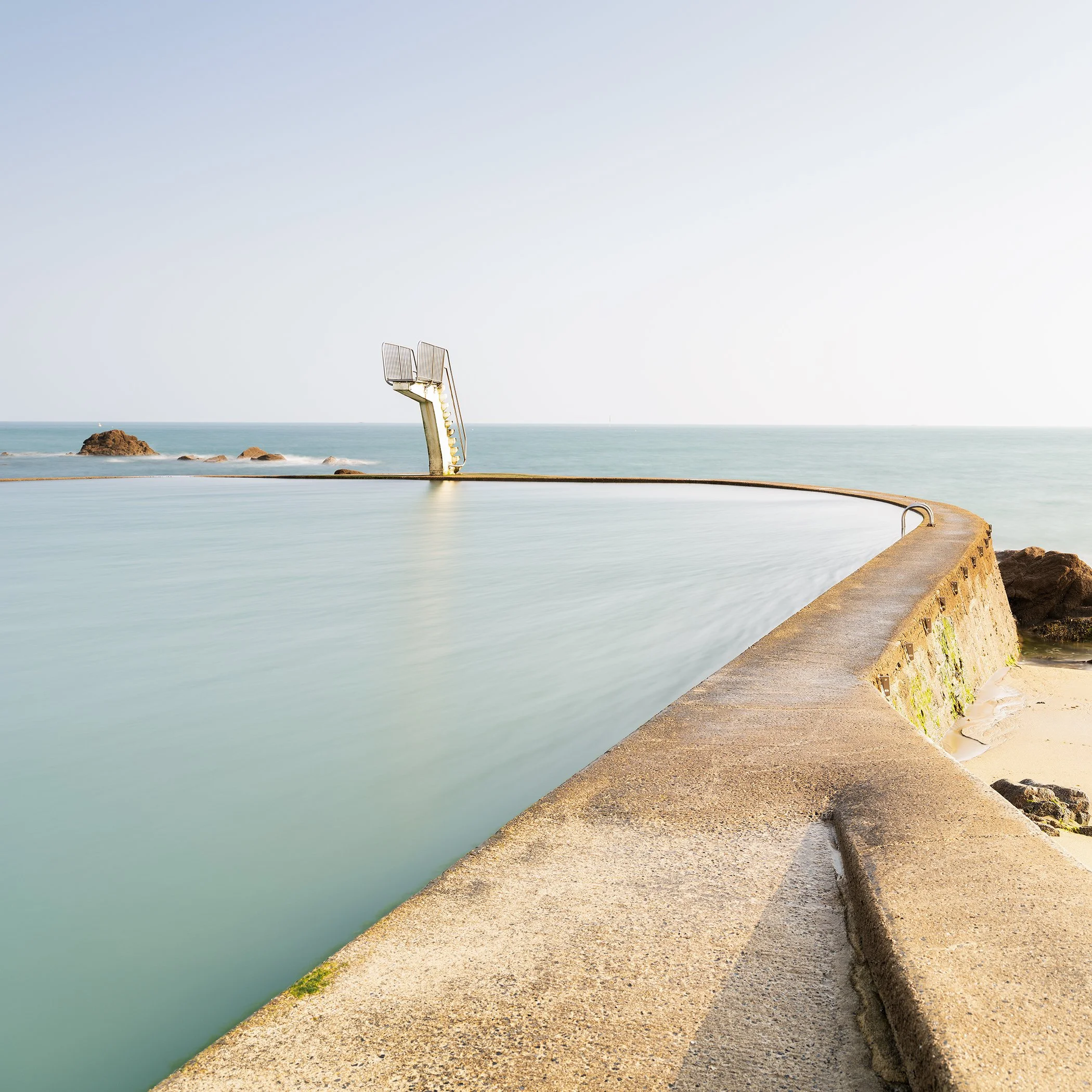 Calm coastal bathing pool beside the open sea with diving board, photo by Gerald Berghammer