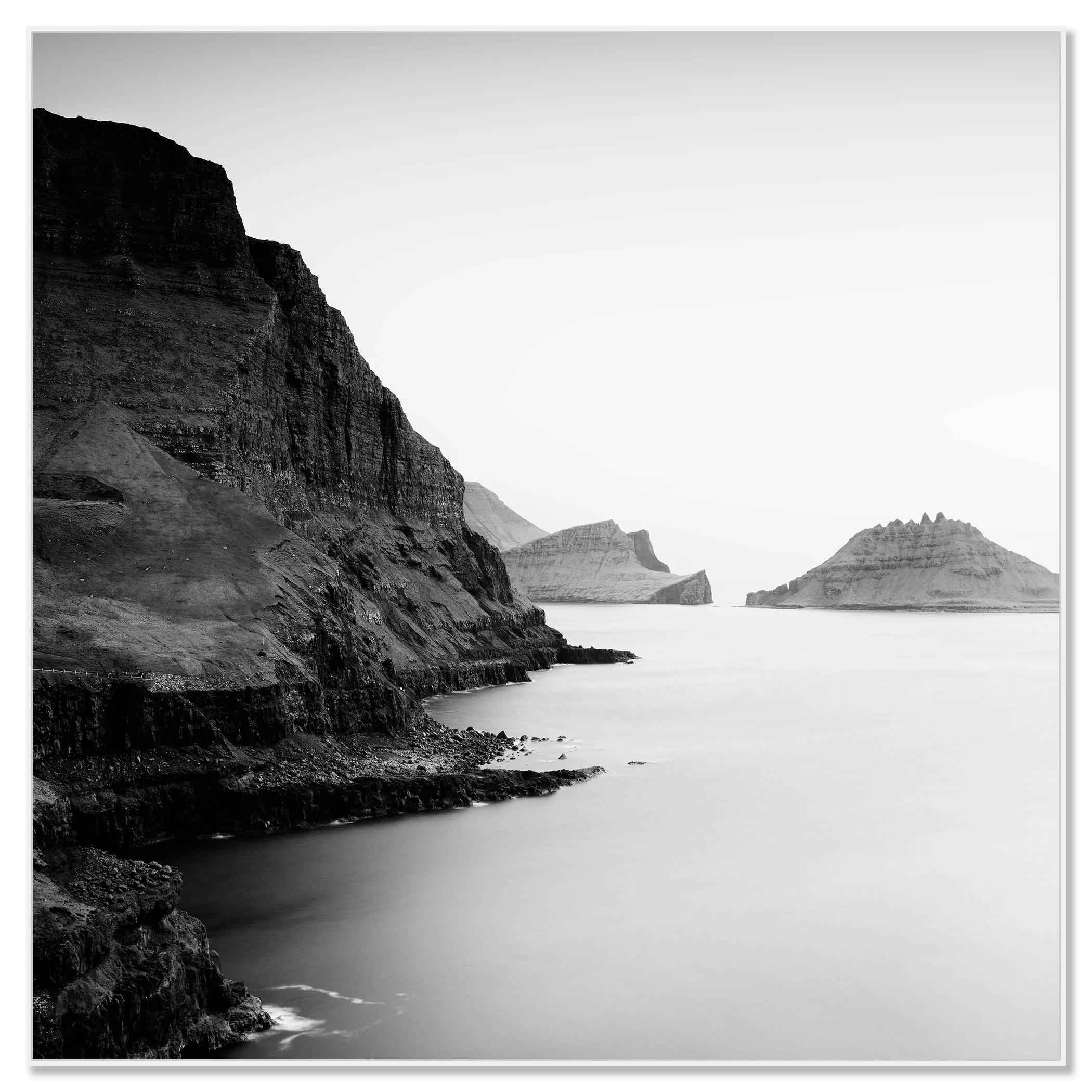 Black and white coastal landscape with steep cliffs, calm sea and distant rocky islands – framed ArtBox white