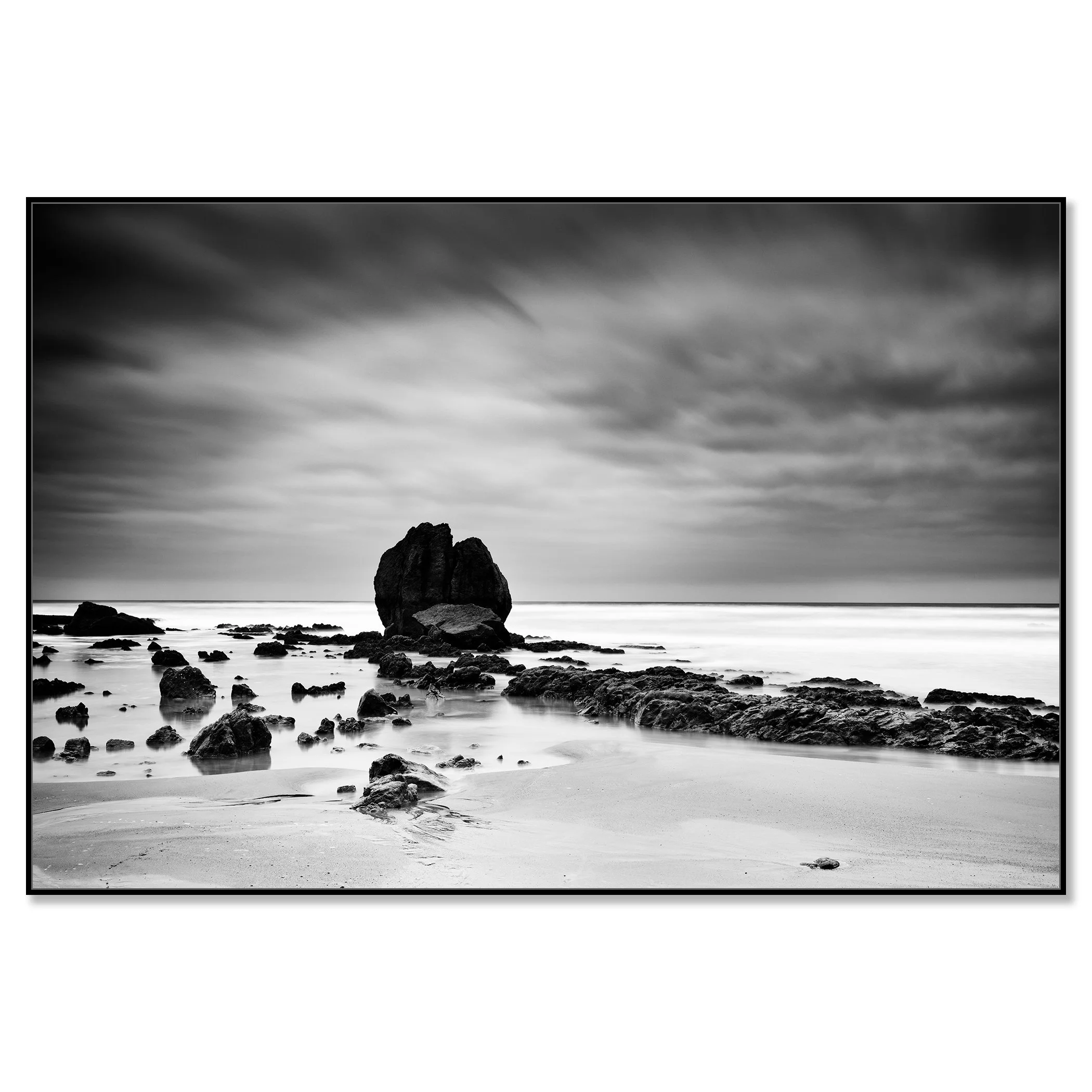 Long-exposure monochrome photo of a rocky beach, soft waves and overcast sky creating a moody seascape – framed ArtBox black