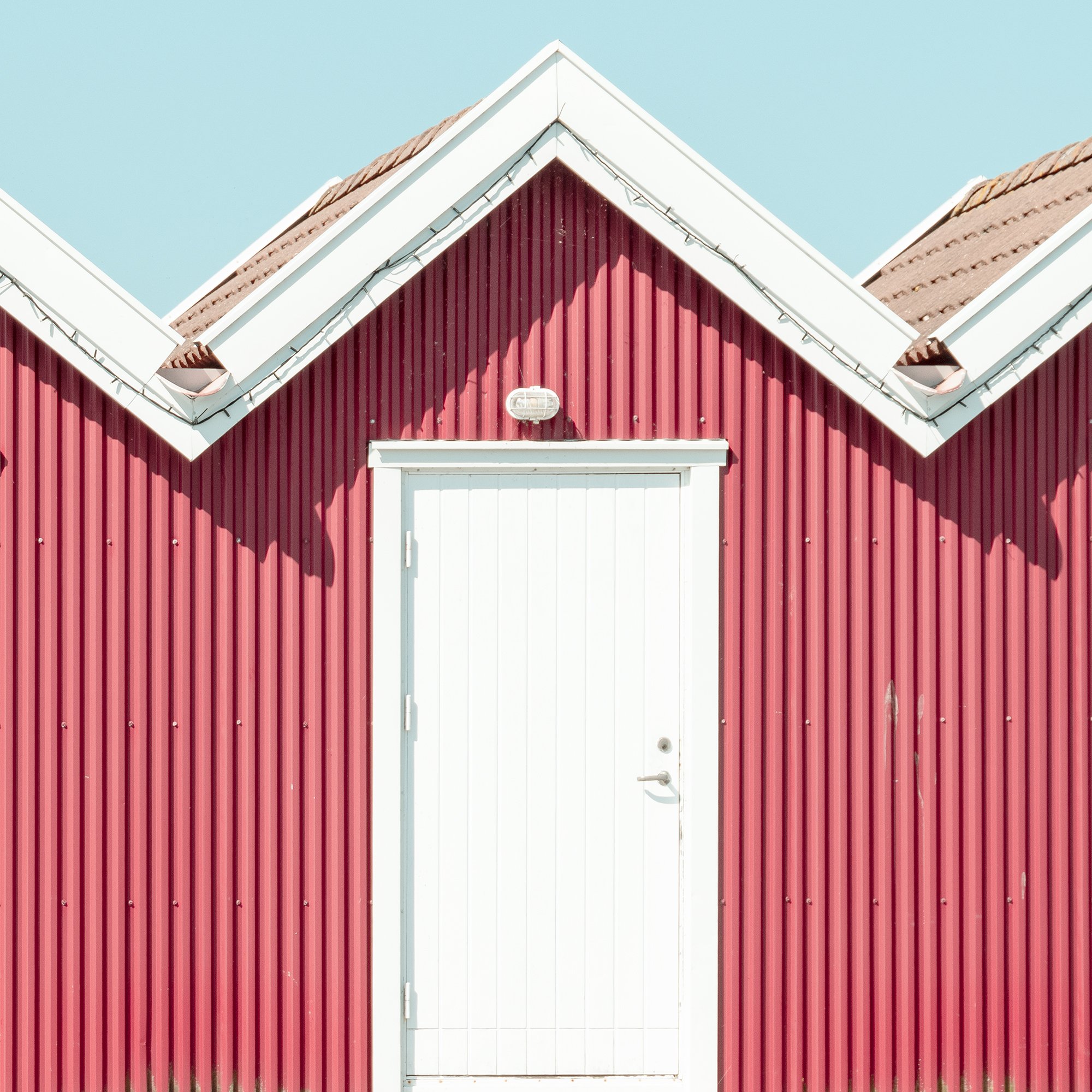 Detailed view of Red Beach Huts Study 1 showing red timber beach huts beneath a clear blue sky in Sweden.