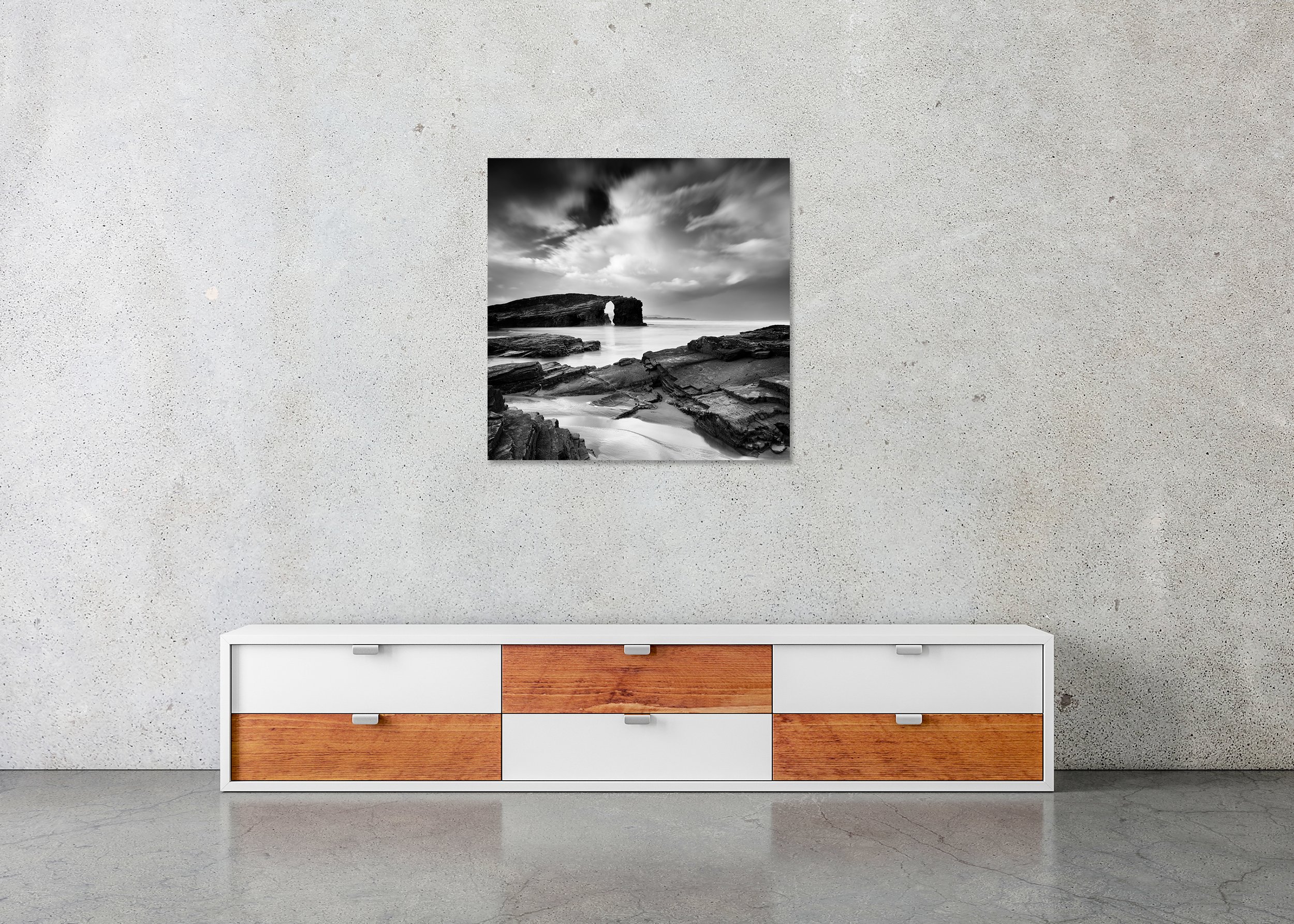 Black and white photo print of a rocky beach with a natural sea arch, calm water and dark clouds, mounted to Dibond without a frame