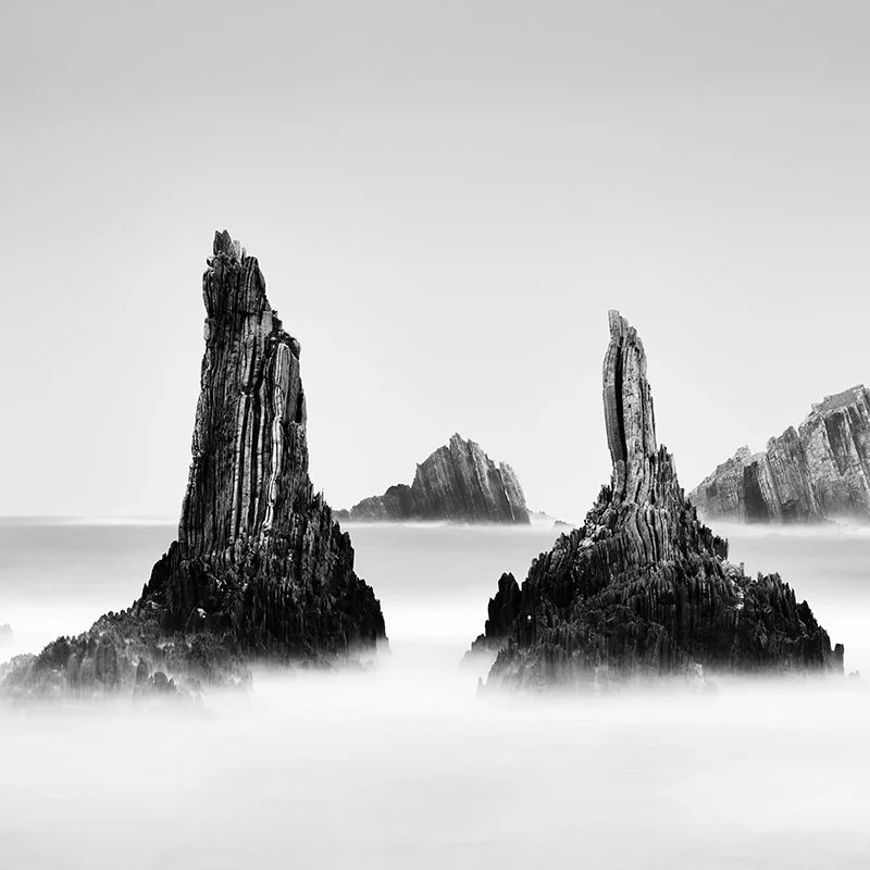 Rocky Peaks Study 2 by Gerald Berghammer, black-and-white long-exposure photograph of jagged sea stacks rising from misty Atlantic water in Spain.