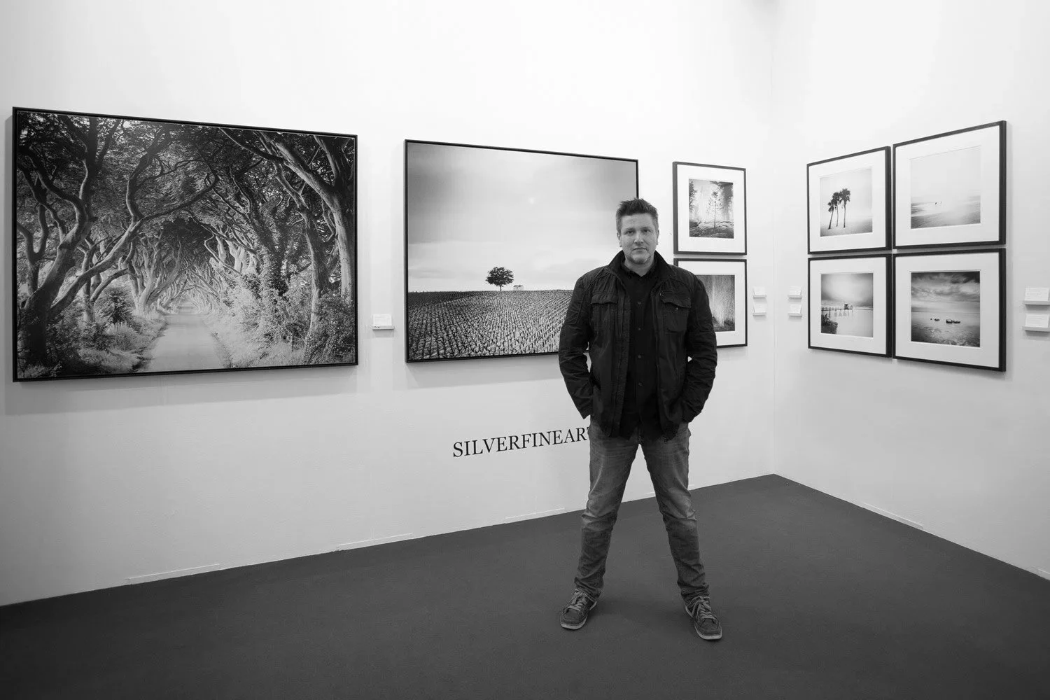 Gerald Berghammer standing in front of large black-and-white landscape photographs by Gerald Berghammer at the SILVERFINEART exhibition, art KARLSRUHE 2017.